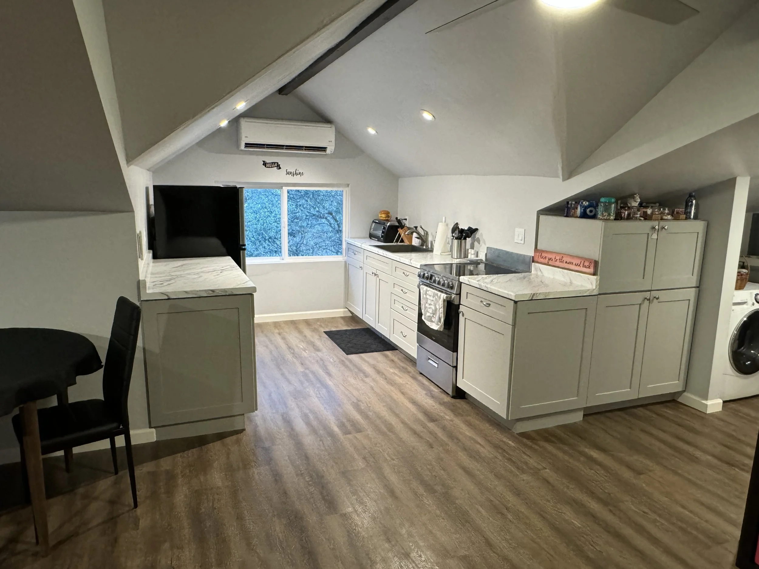 Kitchen with white cabinets, gray countertops, a stove, a window showing a tree outside, and a washer/dryer on the right.