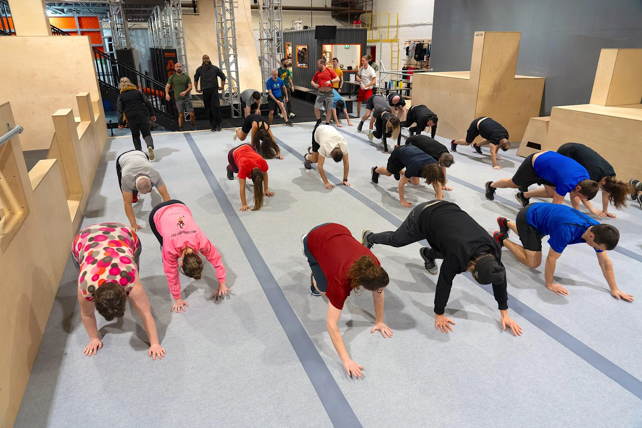 Groupe de personnes faisant des exercices physiques dans une salle avec des structures en bois.
