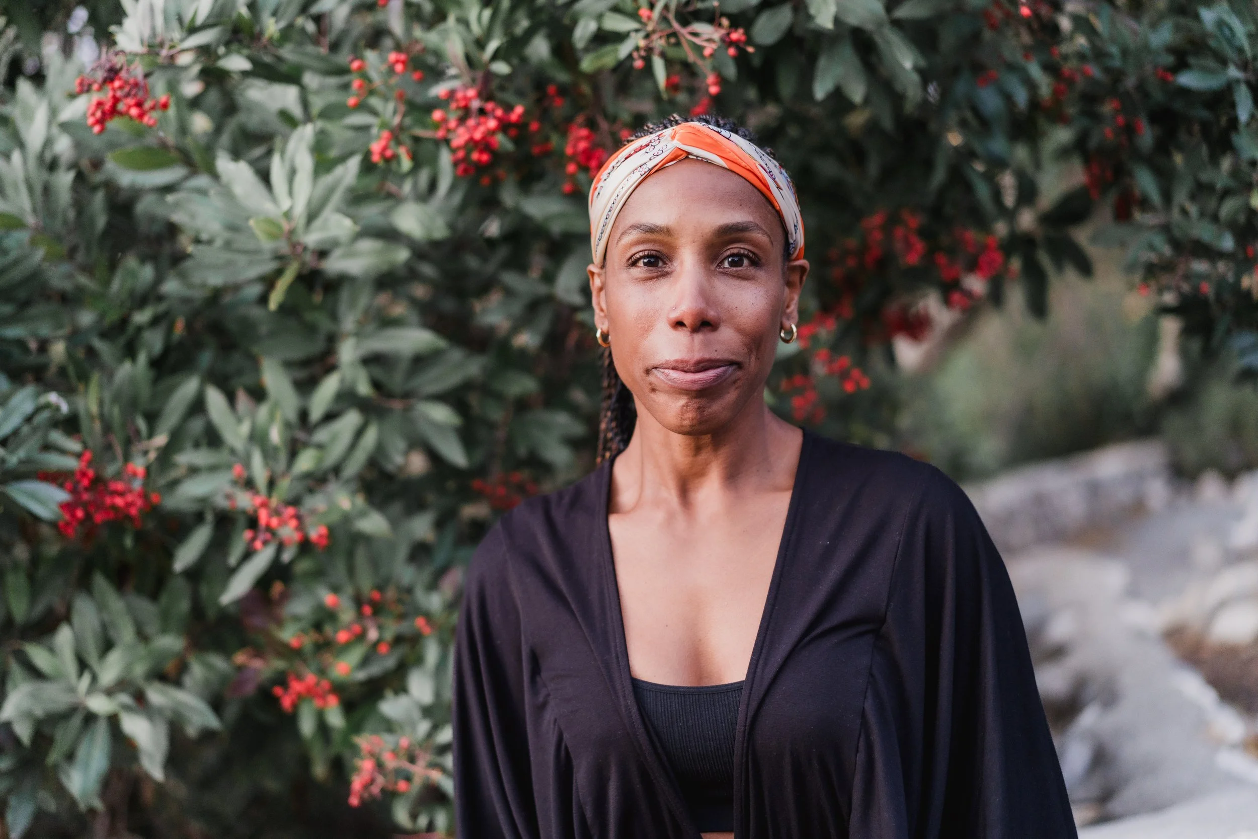 A woman speaking or presenting in a dimly lit indoor setting, wearing a dark athletic top, with one hand raised and the other touching her chest.