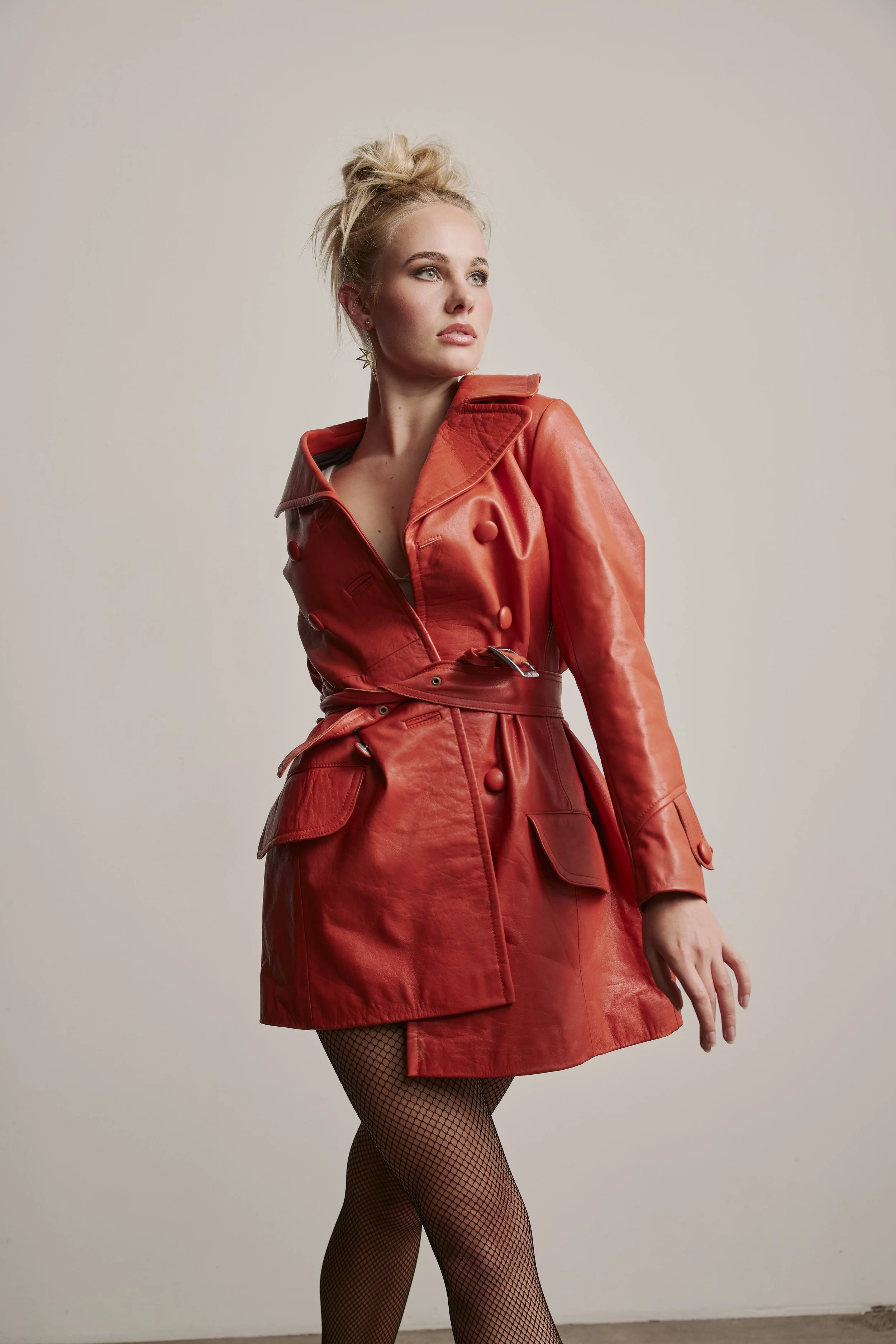 A dancer with her hair in a high messy bun,  wearing laduca dance shoes and fish nets and a vintage orange leather coat 