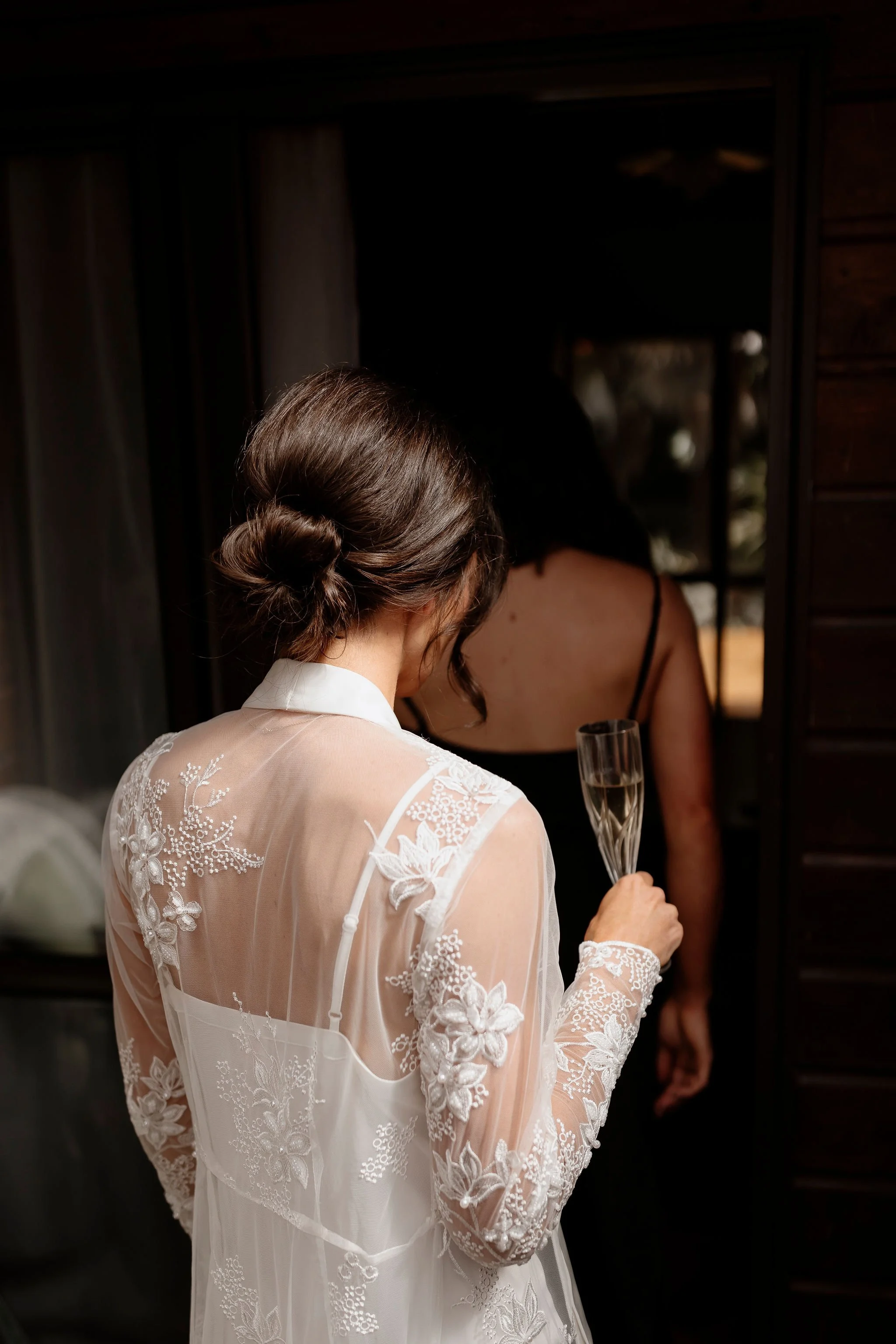 A woman dressed in a lace robe holding a glass of champayne showing the view of her low bun in her hair 