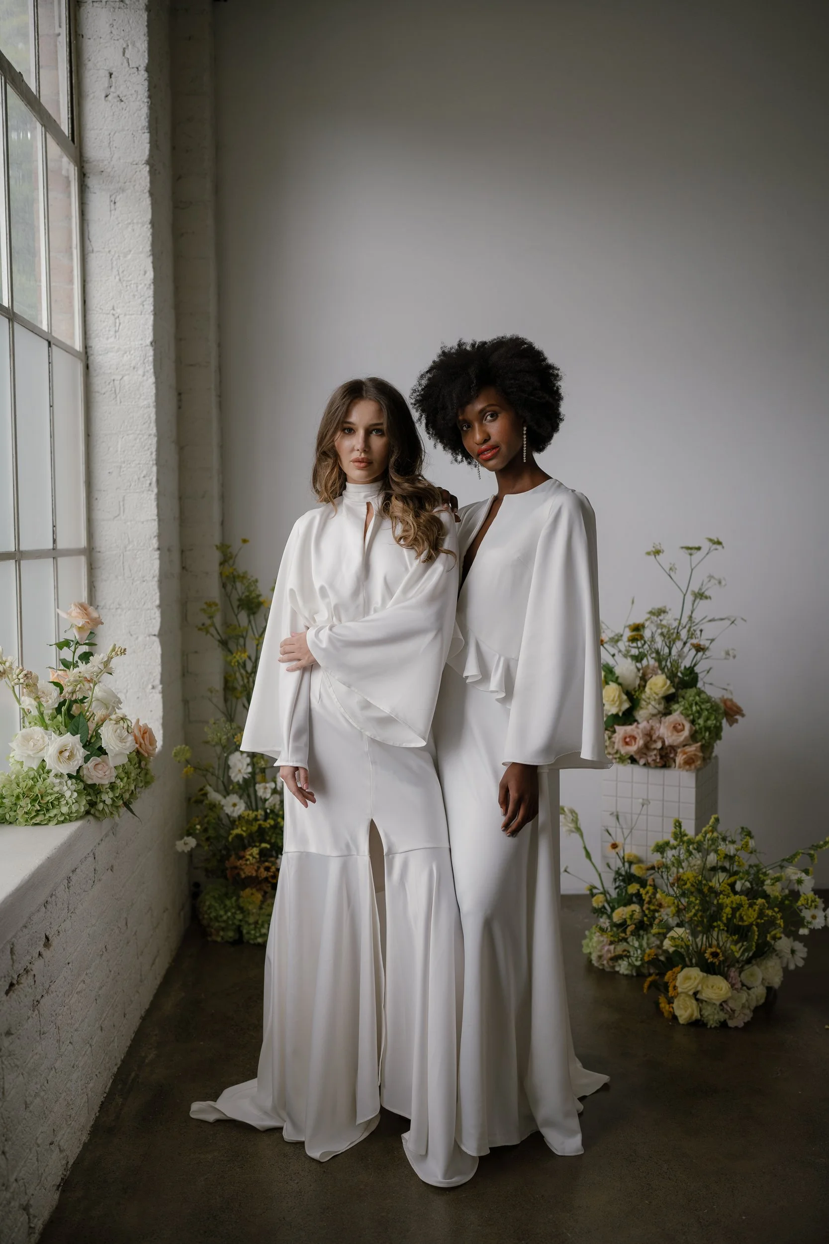 two models posing both wearing white lookings very chic.one model had long brunette hair the other short black coily hair 