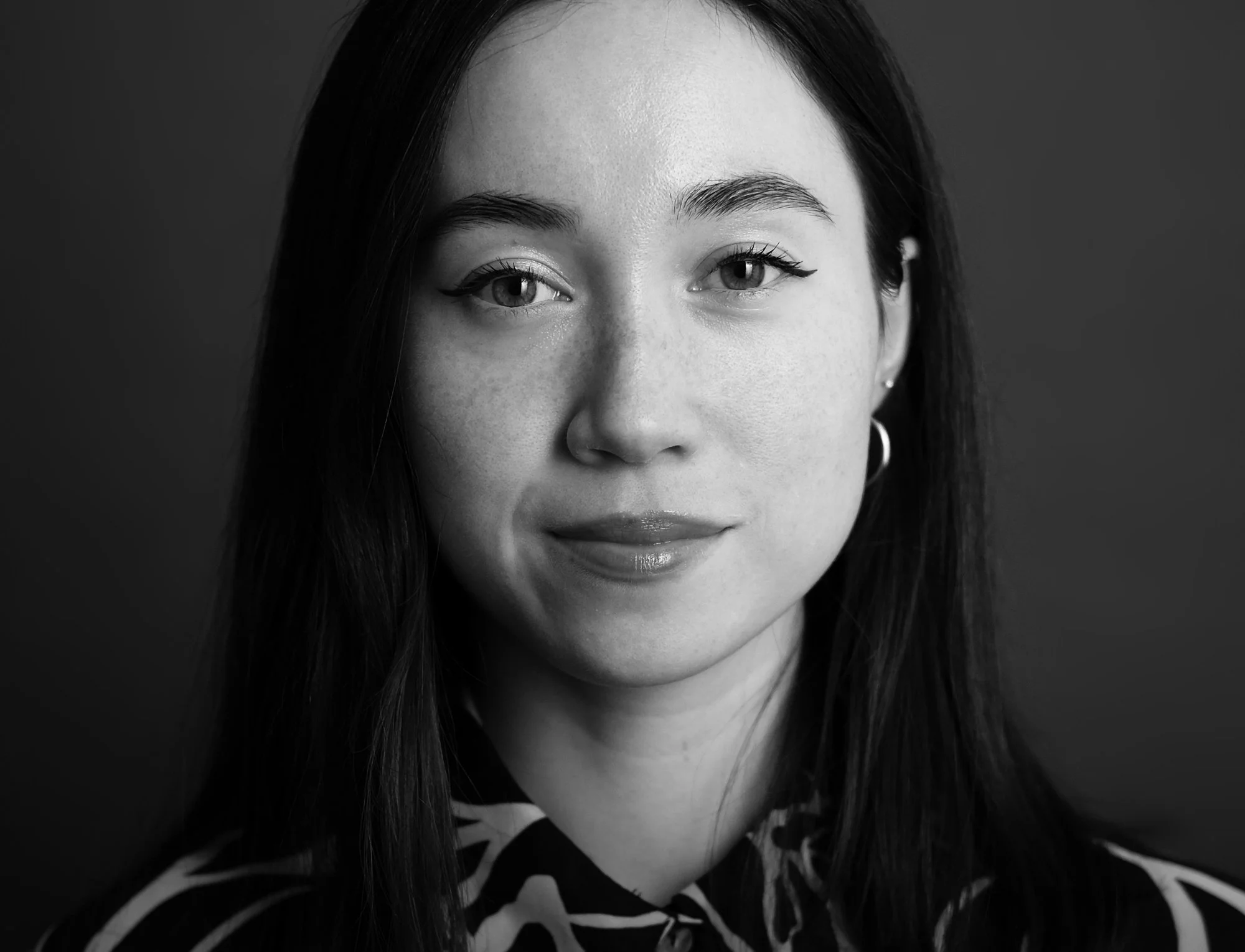 Black and white portrait of a young woman with long dark hair, wearing a patterned top, and looking directly at the camera.