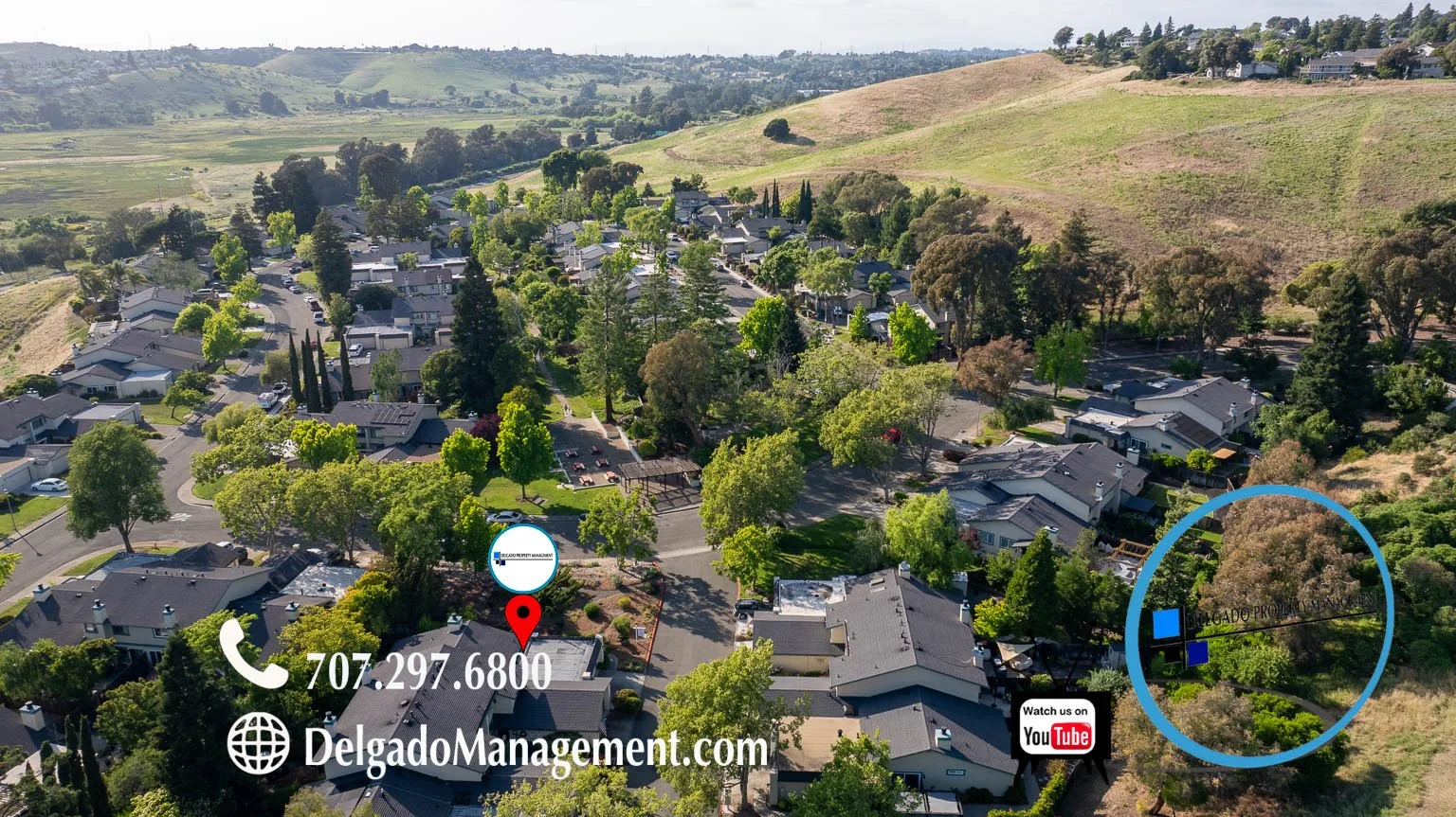 Aerial view of a residential neighborhood with houses, trees, and a park, overlooking rolling hills and open land.
