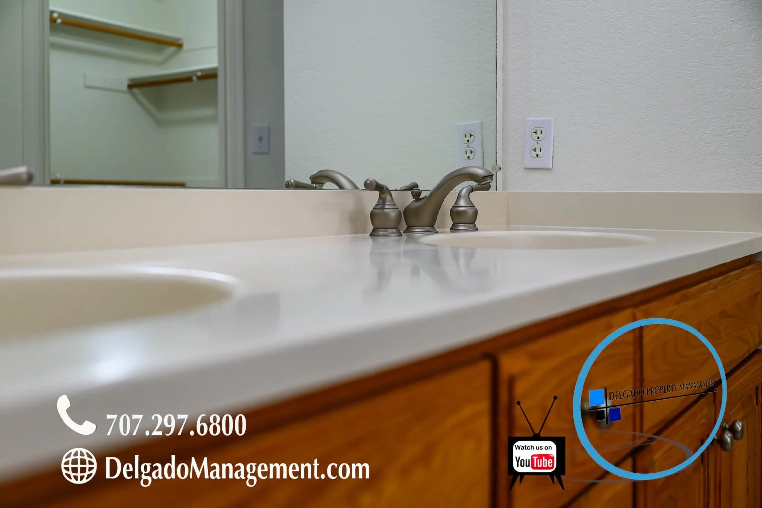 Bathroom sink with beige countertop, two silver faucets, wood cabinet, mirror, and electrical outlets on the wall.