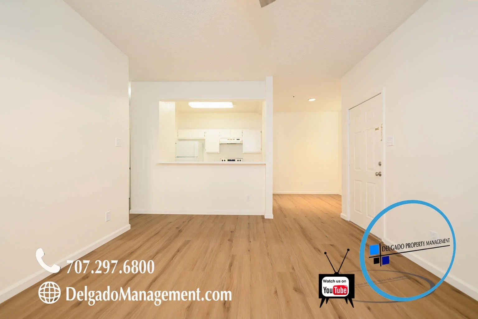 Empty living room with wooden floors, white walls, view into kitchen area, and a door on the right side. Contact info and logos for Delgado Property Management are in the bottom right corner.