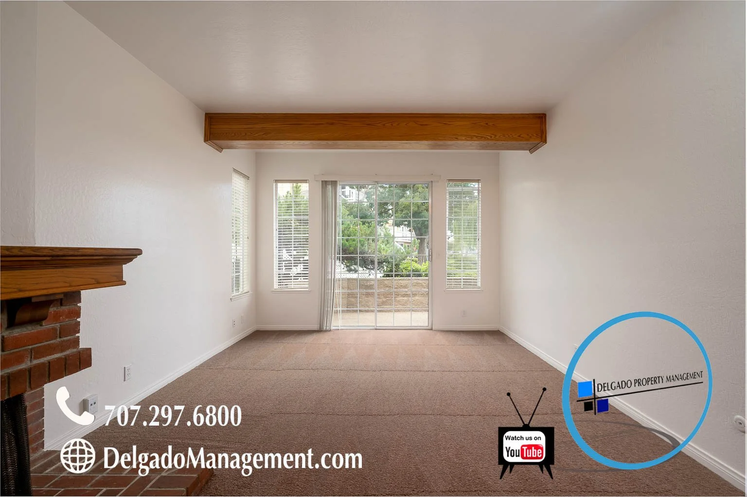 Empty living room with beige carpet, white walls, a brick fireplace on the left, and large windows with a sliding glass door leading to a small outdoor patio, advertising Delgado Property Management with contact info and YouTube logo.
