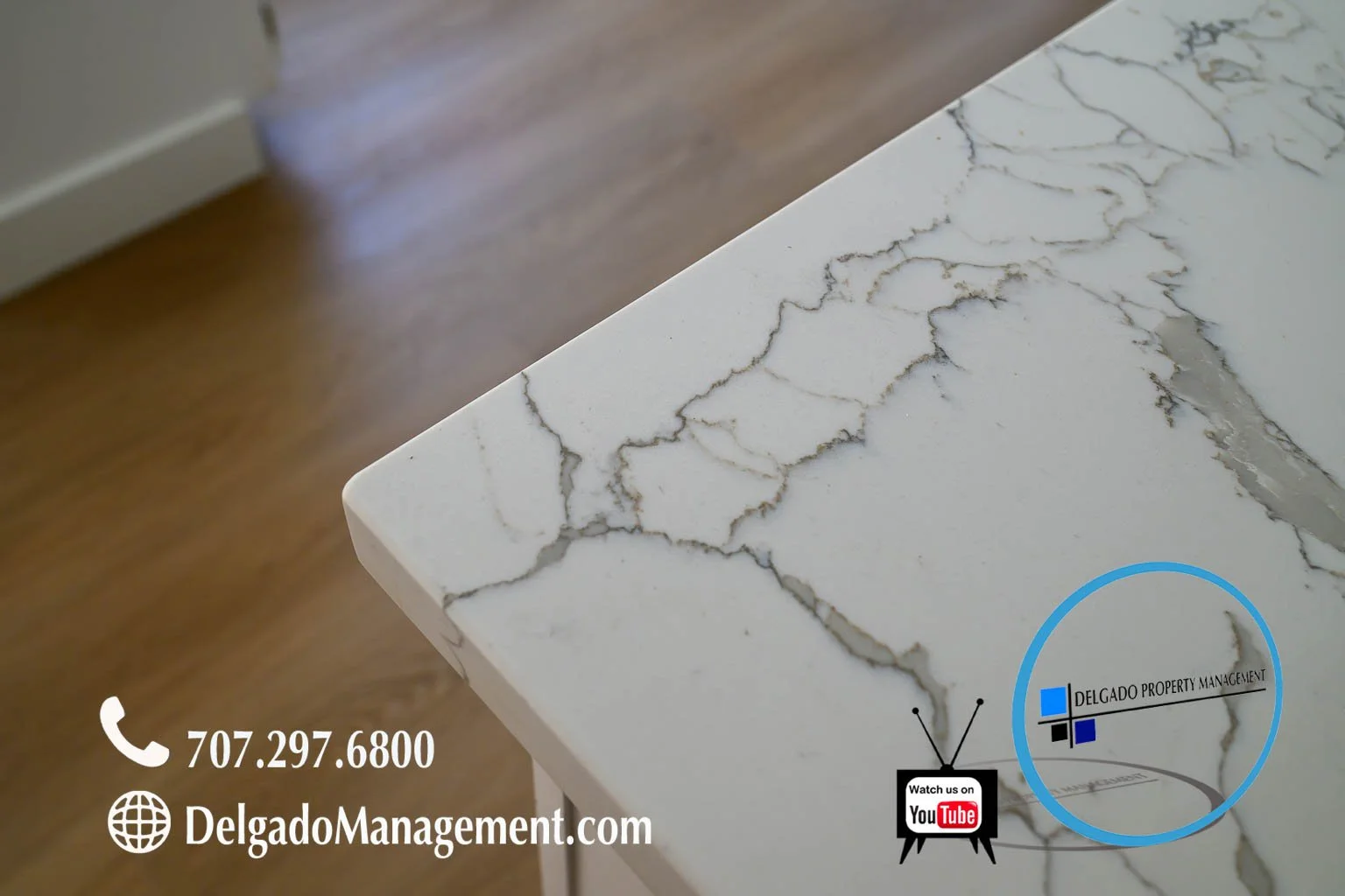 Close-up of a white marble countertop with gray veining, showing contact information and social media icons for Delgado Property Management.