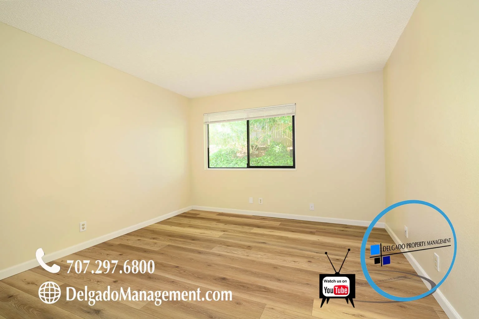 Empty room with wood flooring, cream-colored walls, a window showing green foliage, and logos for Delgado Property Management and YouTube, along with a phone number and website.