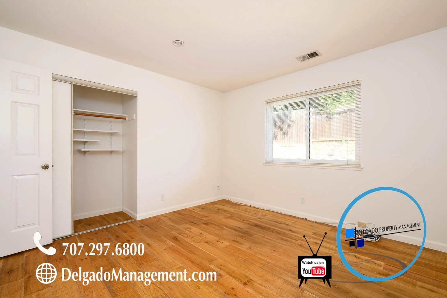 Empty bedroom with hardwood floors, white walls, a window with blinds, an open closet with shelves, and furniture placement overlay in the corner.