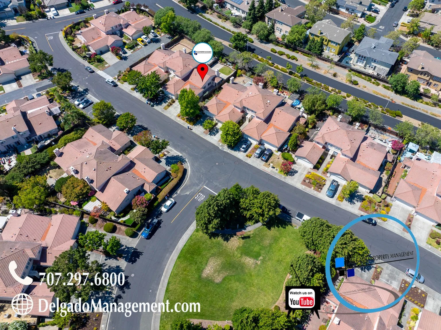 Aerial view of a residential neighborhood with houses, trees, and cars parked along the streets. There is a green park area with a bench, and some markings indicating property management services with contact information.