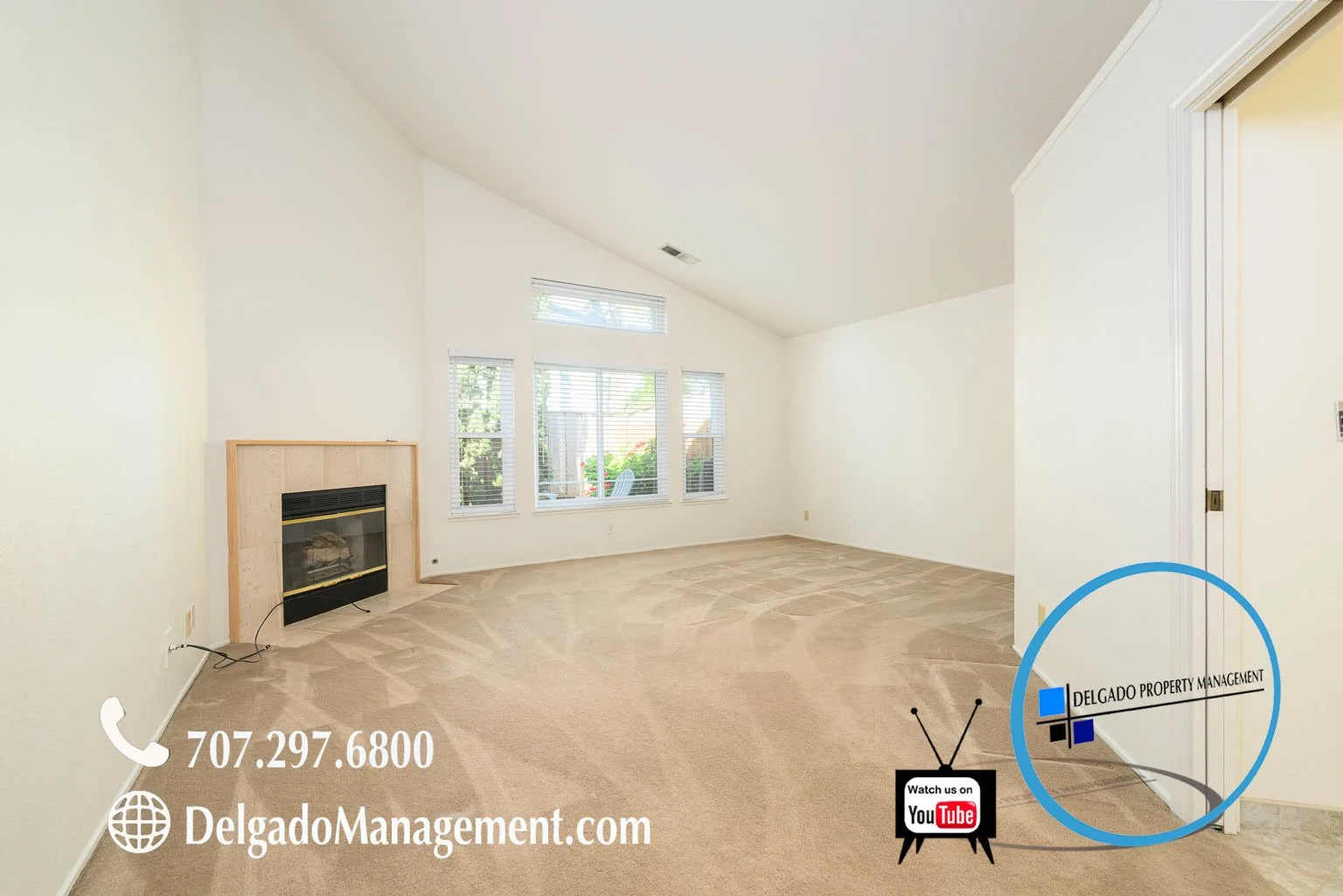 Empty living room with beige carpet, white walls, large window, corner fireplace, and a door, with overlay text for property management contact info and YouTube channel.