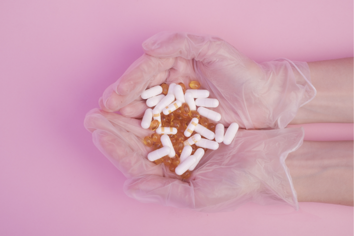 Gloved hands holding a pile of pills on a pink background