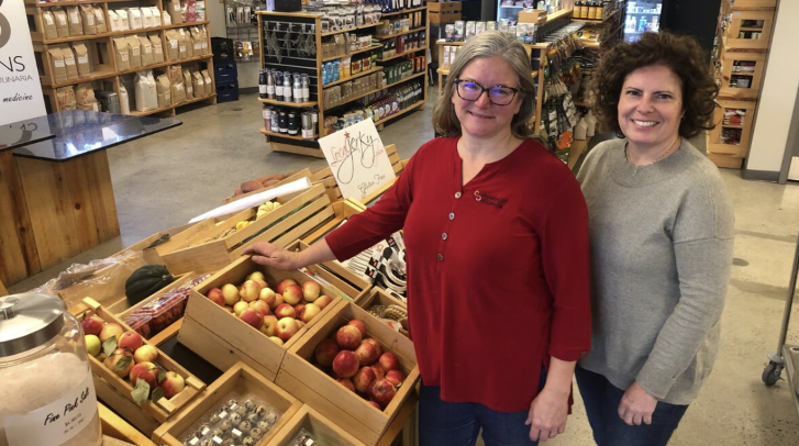 Two pharmacy staff standing beside a fresh produce display