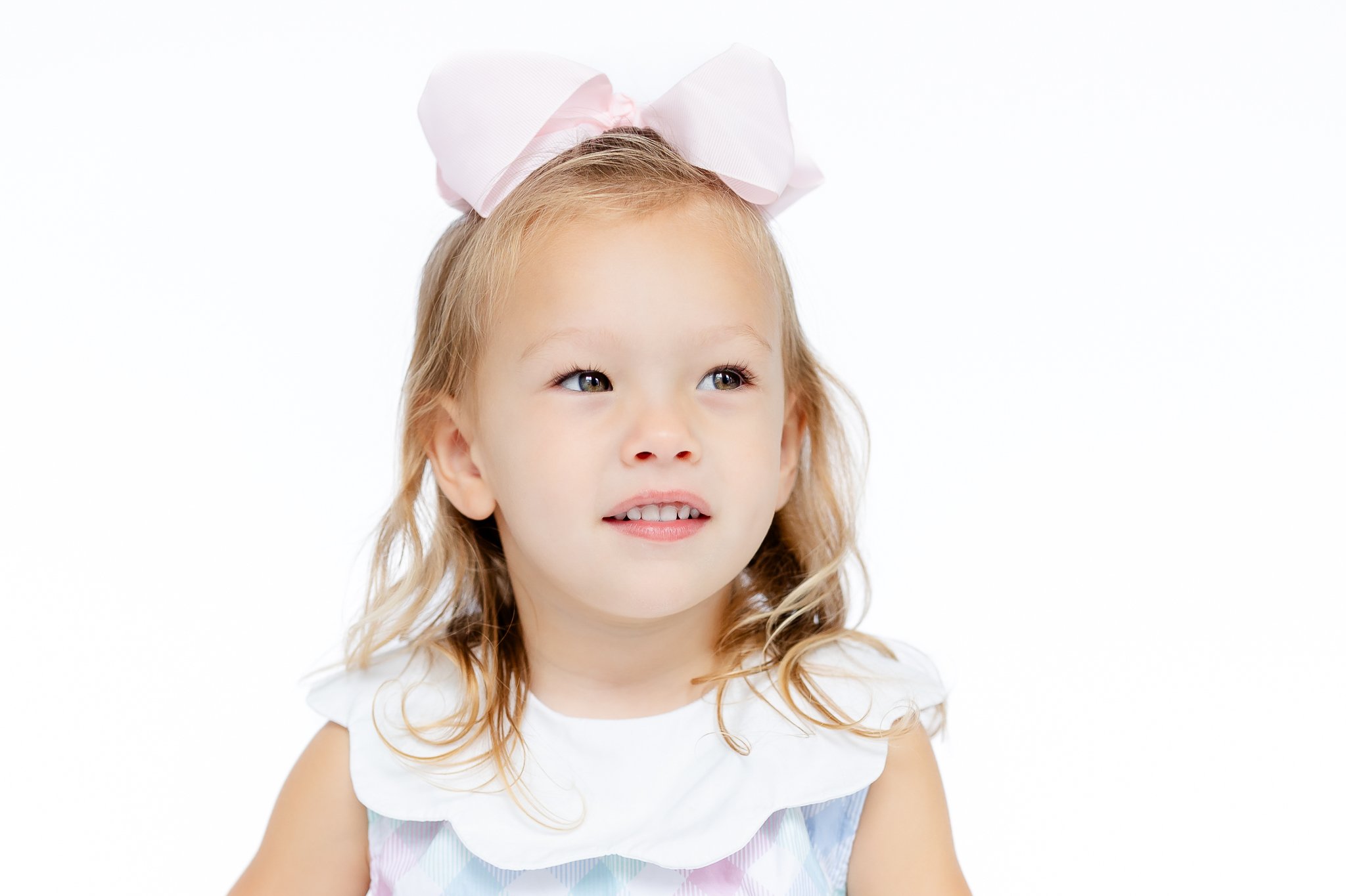 Young child with a pink bow and a colorful dress against a white background.