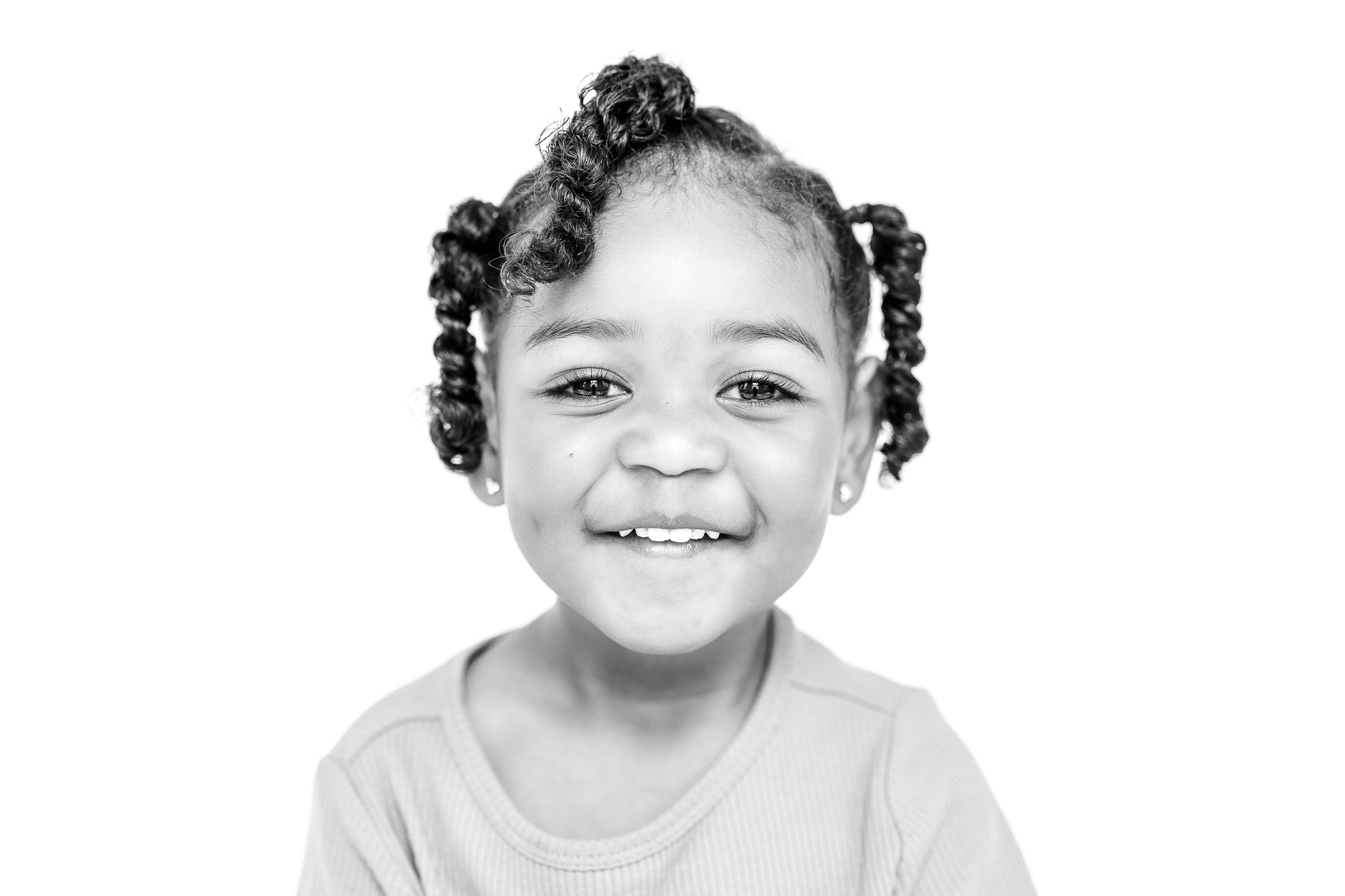 Black and white photo of a smiling child with curly hair and earrings.