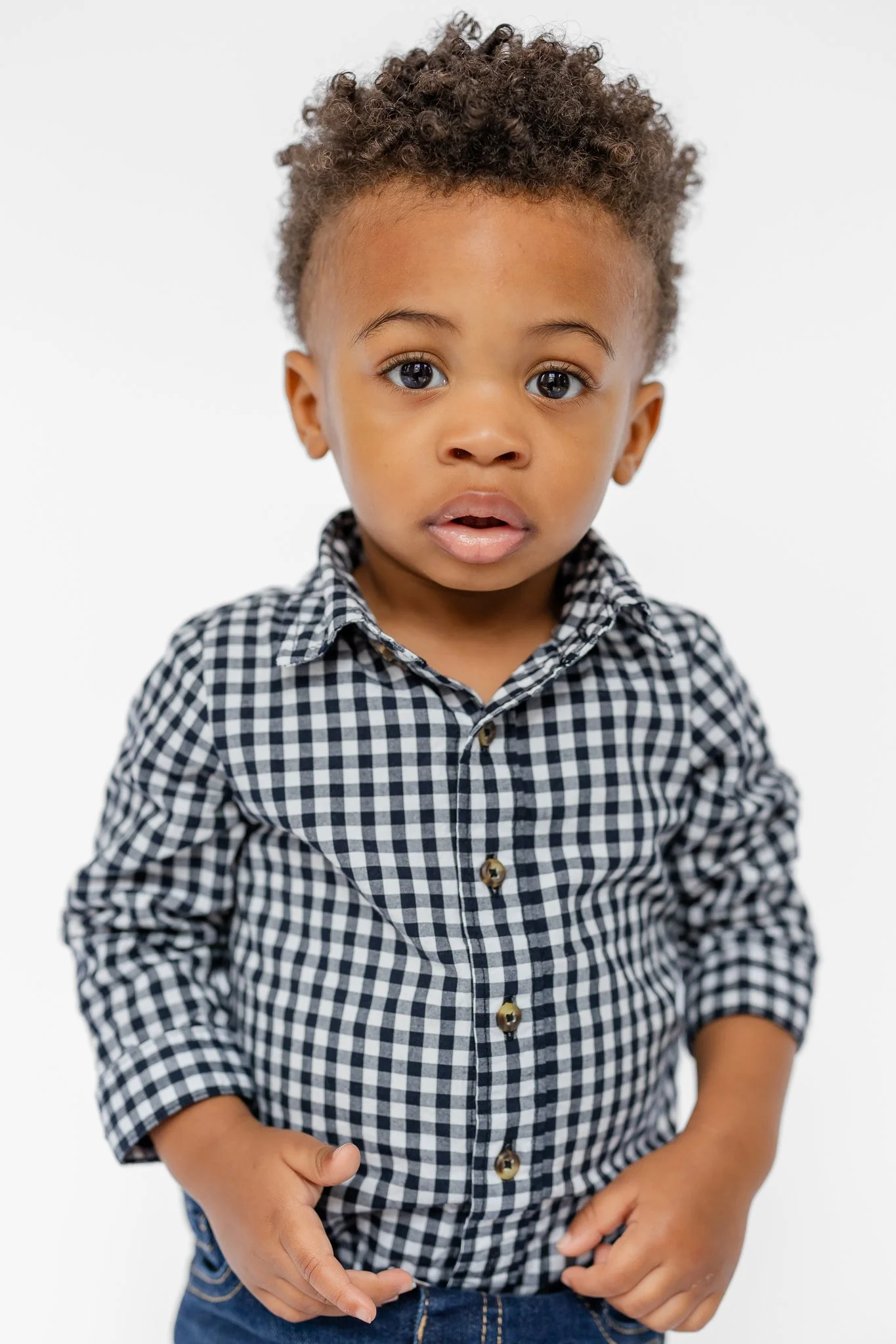 Young child in a black and white checkered shirt with a surprised expression, against a plain background.