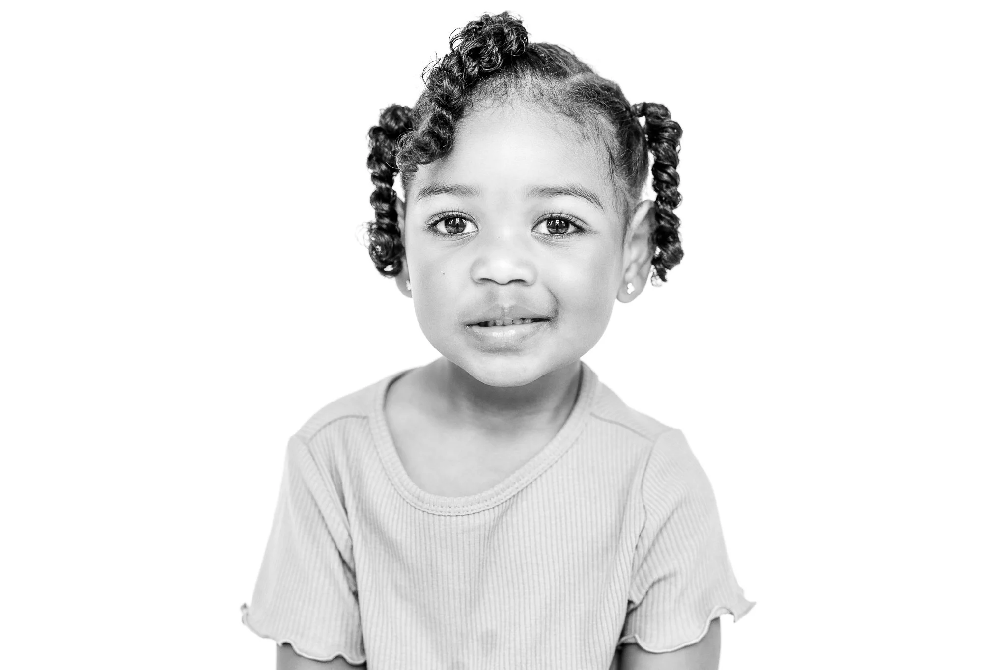 Black and white portrait of a young child with curly hair and a gentle smile, wearing a light-colored shirt.