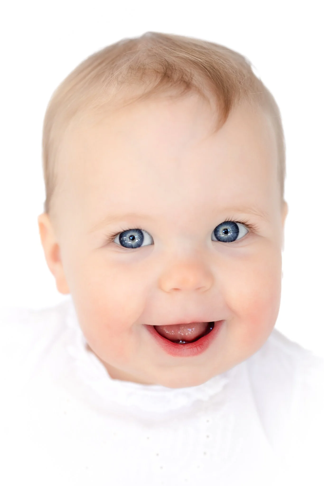 Smiling baby with blue eyes and light hair in white clothing, close-up.