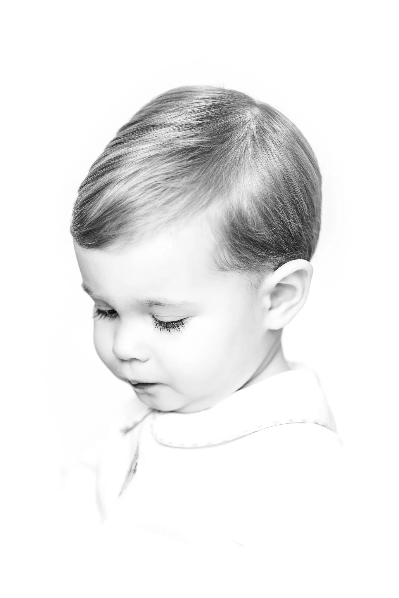 Black and white portrait of a young child with short hair, looking down with closed eyes.