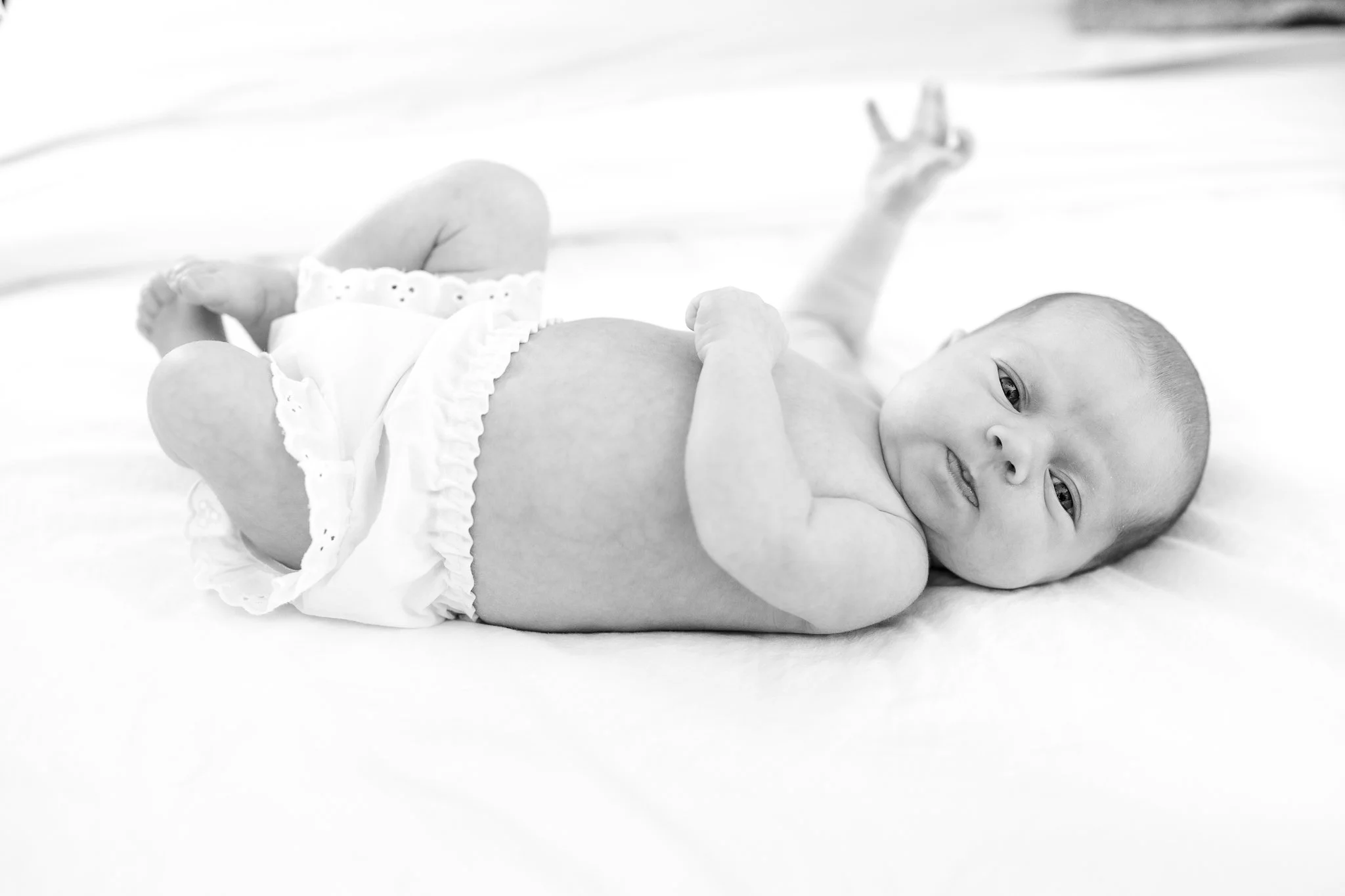 Black and white photo of a newborn baby lying on a bed, wearing white diaper covers.