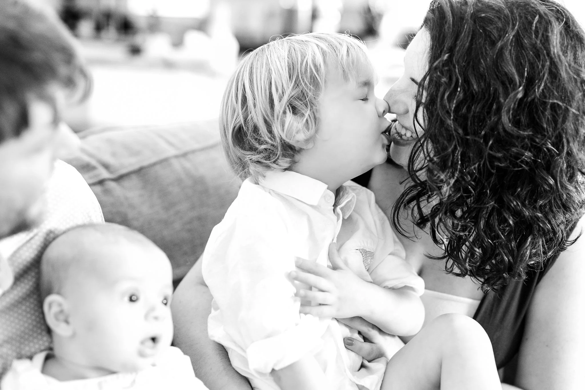 Black and white photo of a family with a child kissing an adult, another adult holding a baby on a couch.