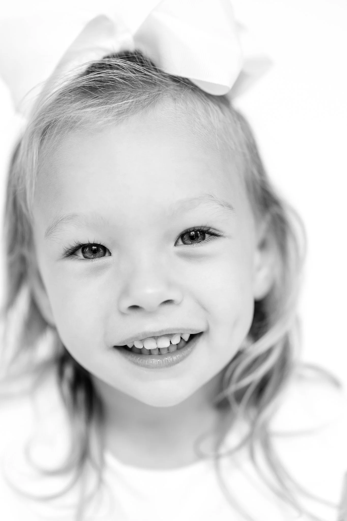 Black and white portrait of a young child with a large bow, smiling.