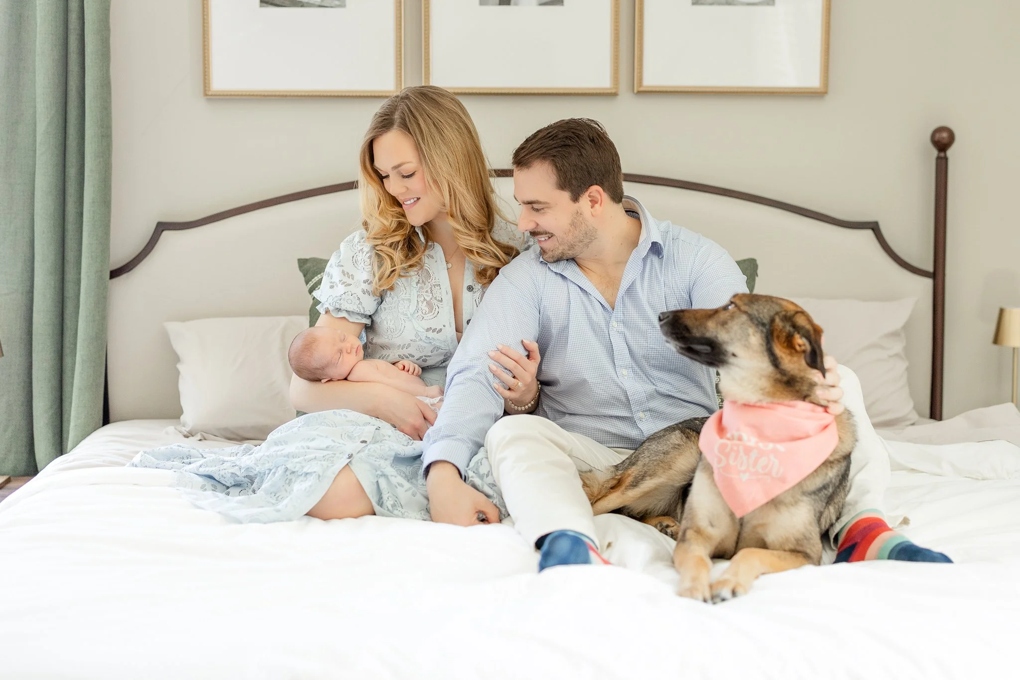 Family with newborn and dog on bed, woman holding baby.