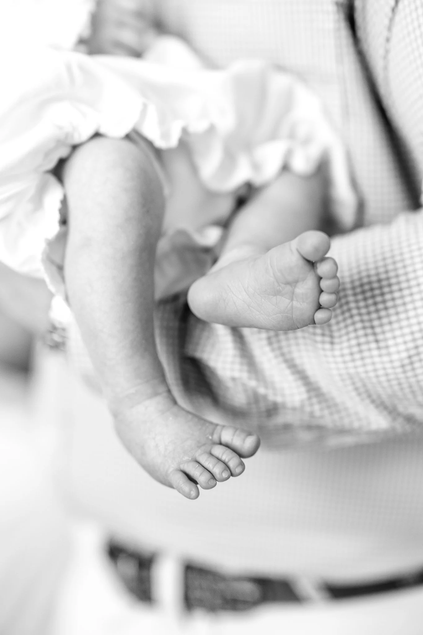 Black and white image of a baby's feet, held by an adult, with the baby wearing a ruffled garment.