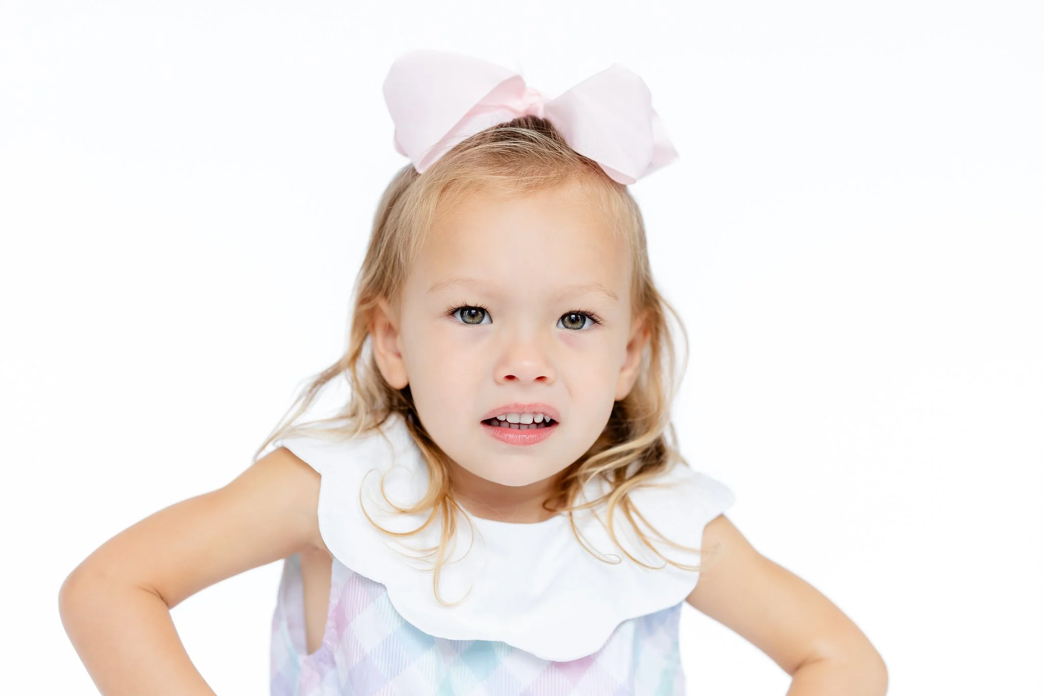 Young girl with a large pink bow in her hair, wearing a white-collared dress, looking directly at the camera.
