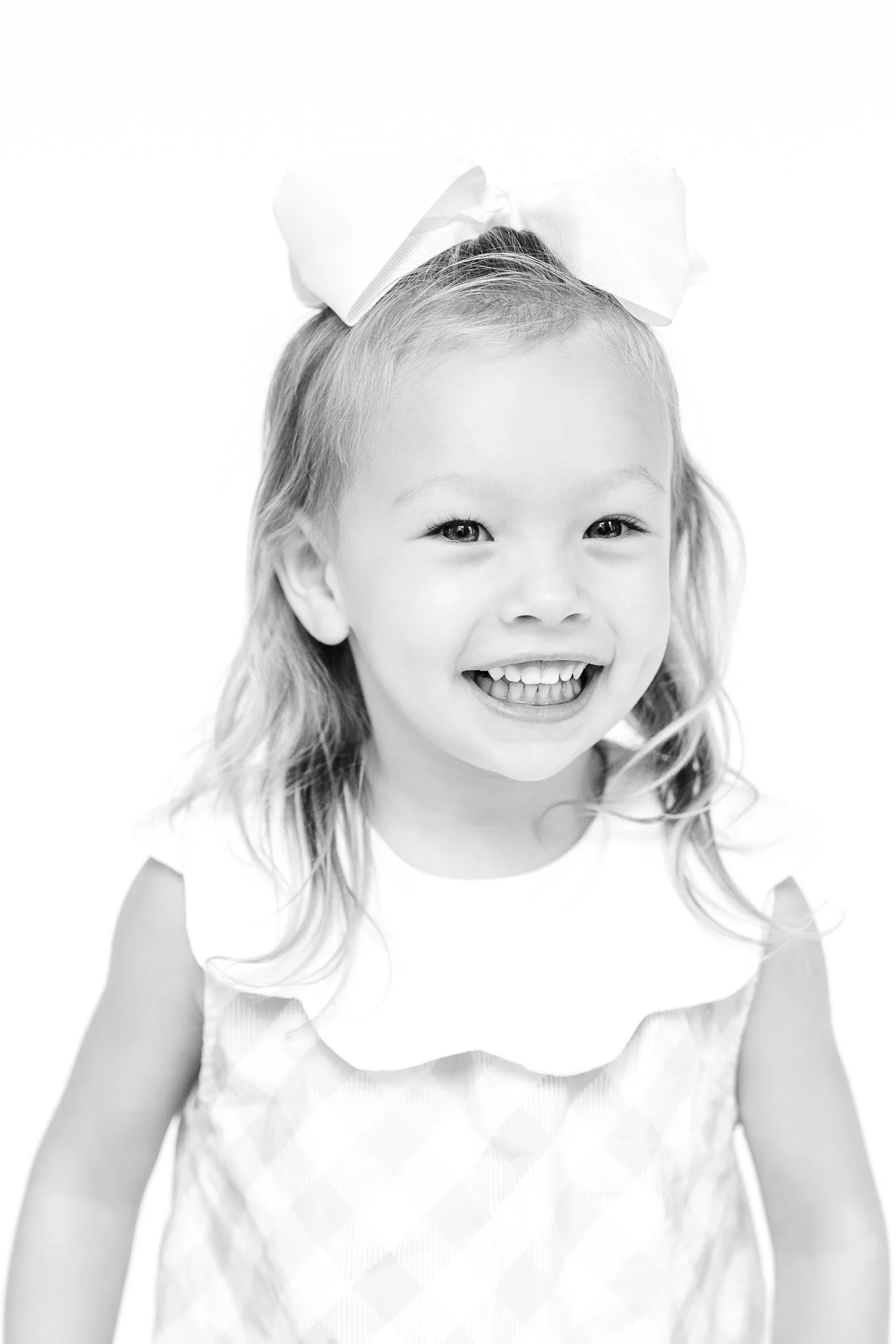 Black and white photo of a smiling young girl with long hair and a bow