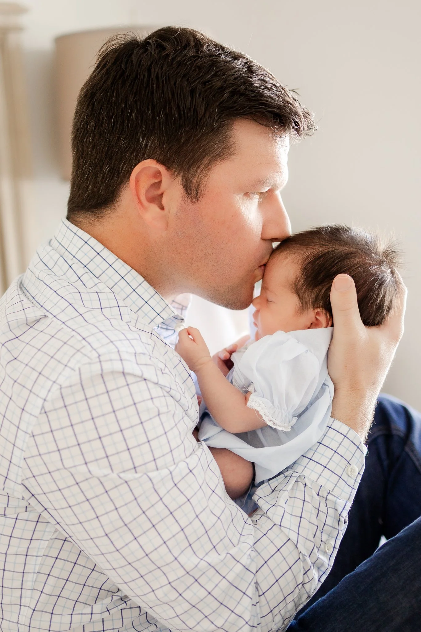 Man tenderly kissing a baby's forehead indoors.