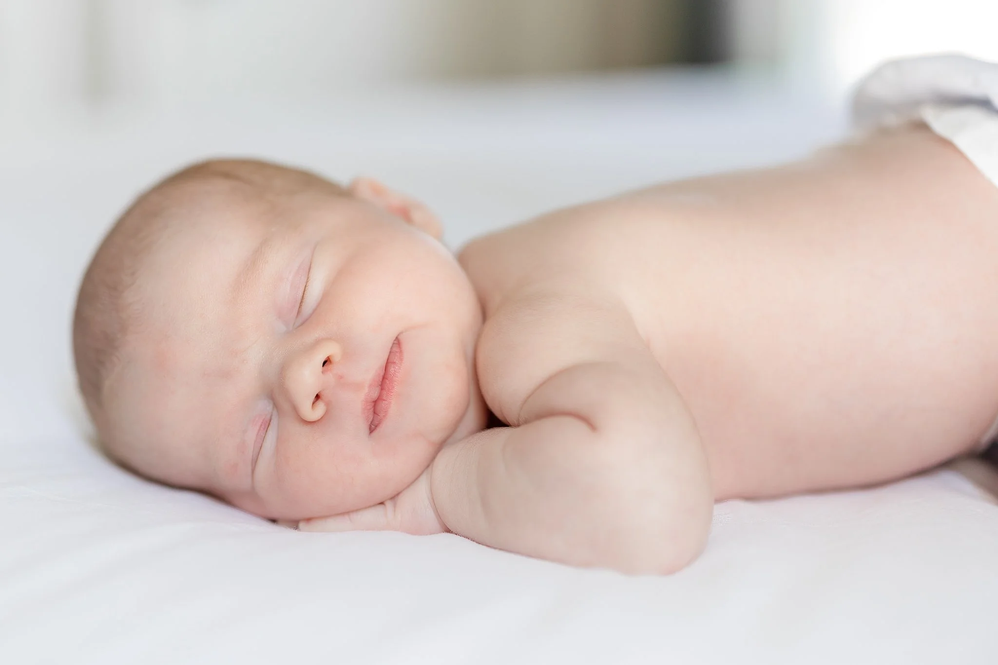 Sleeping newborn baby lying on a white bed.