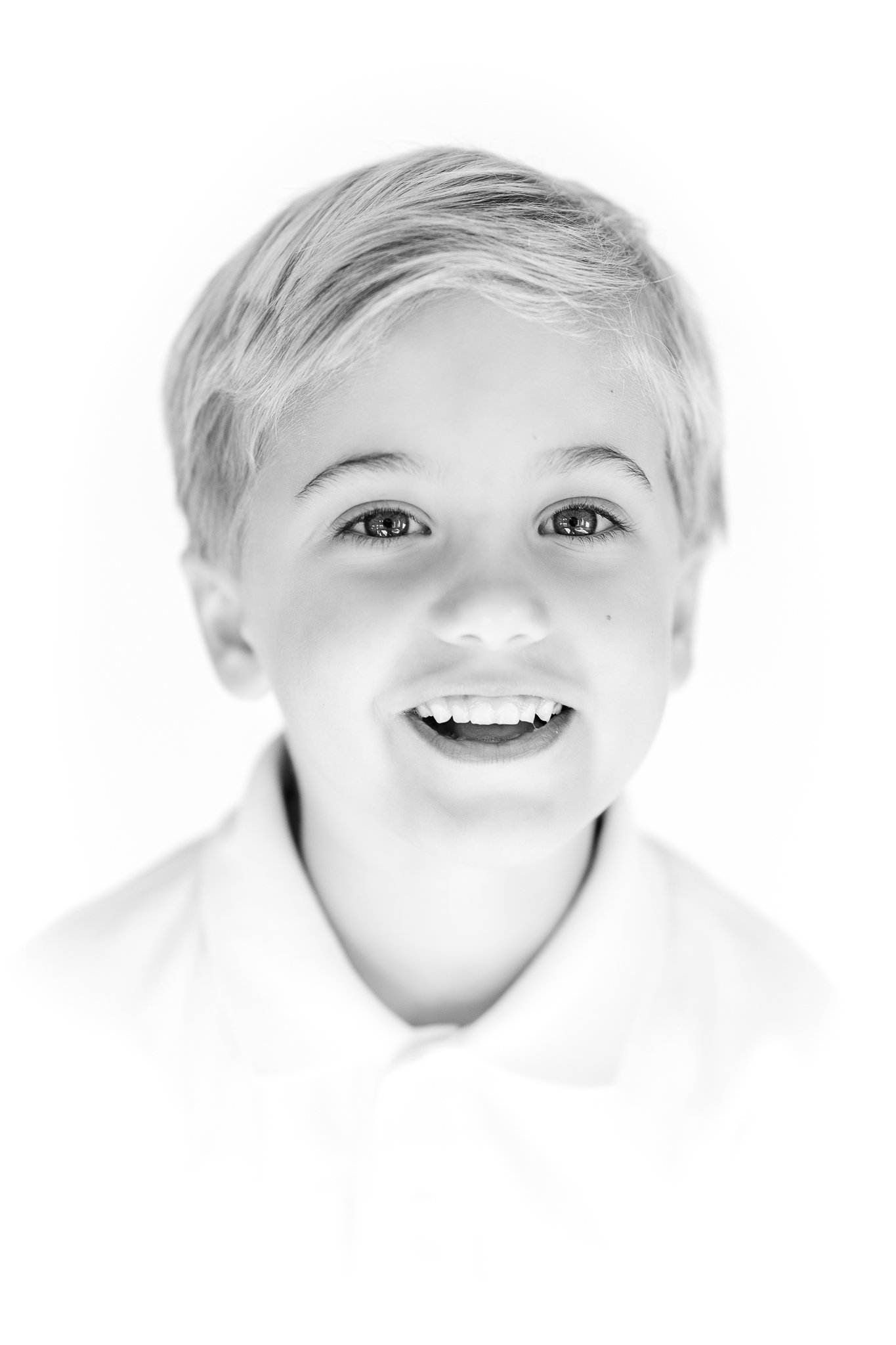 Black and white portrait of a smiling child with light-colored hair, wearing a collared shirt.