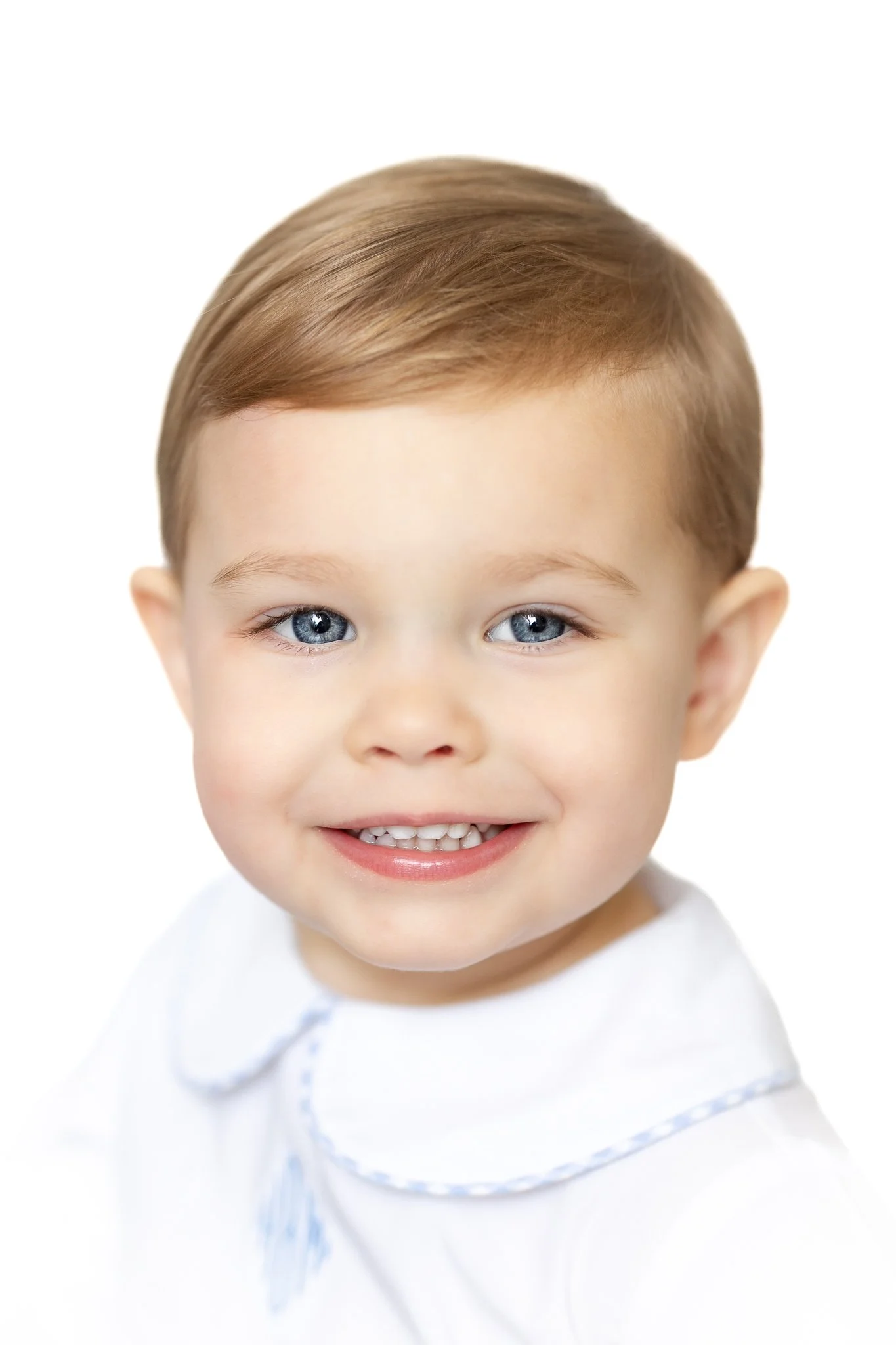 Smiling toddler wearing a white top with a Peter Pan collar.