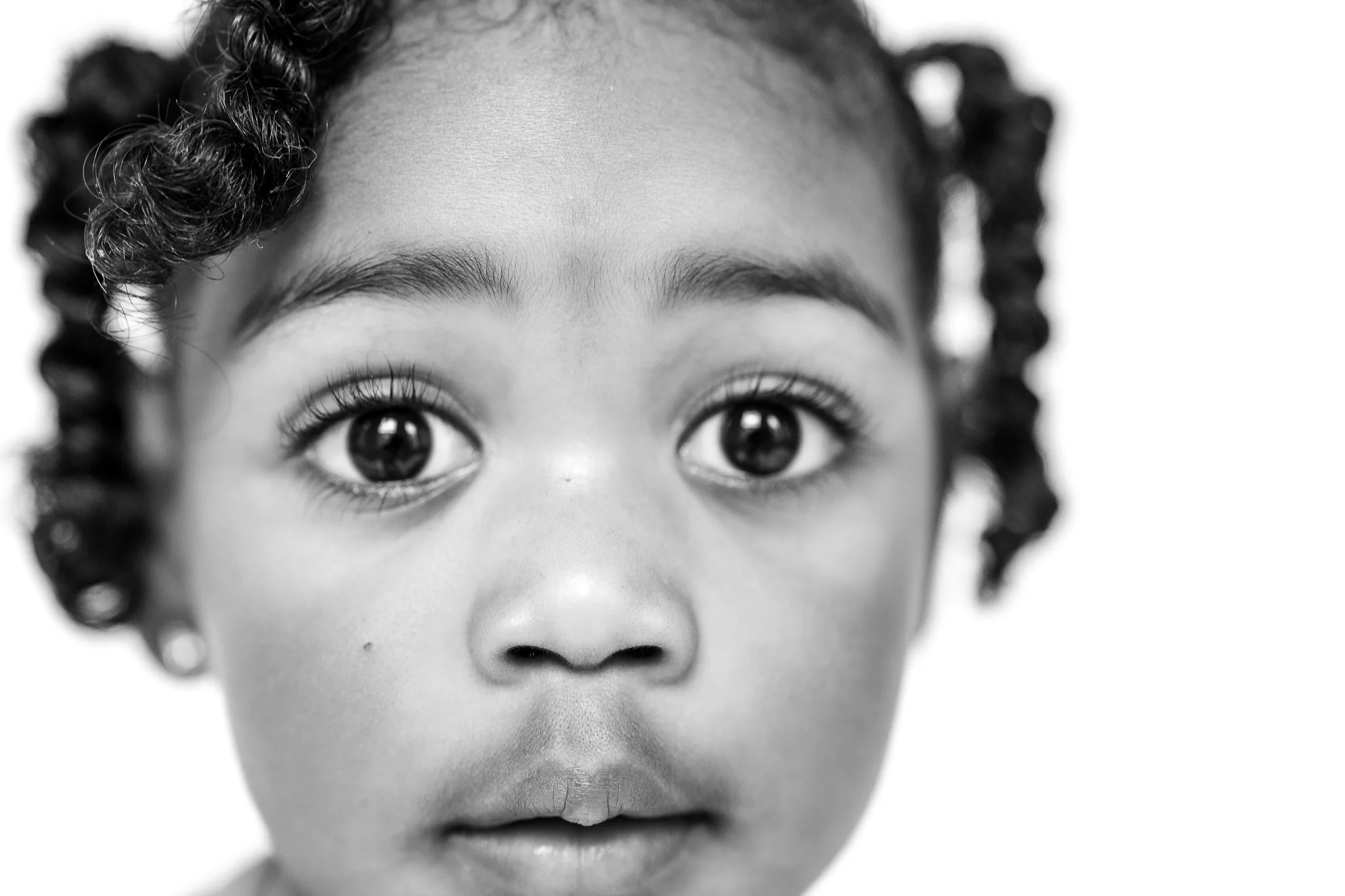 Close-up black and white photo of a child's face with curly hair and wide eyes.