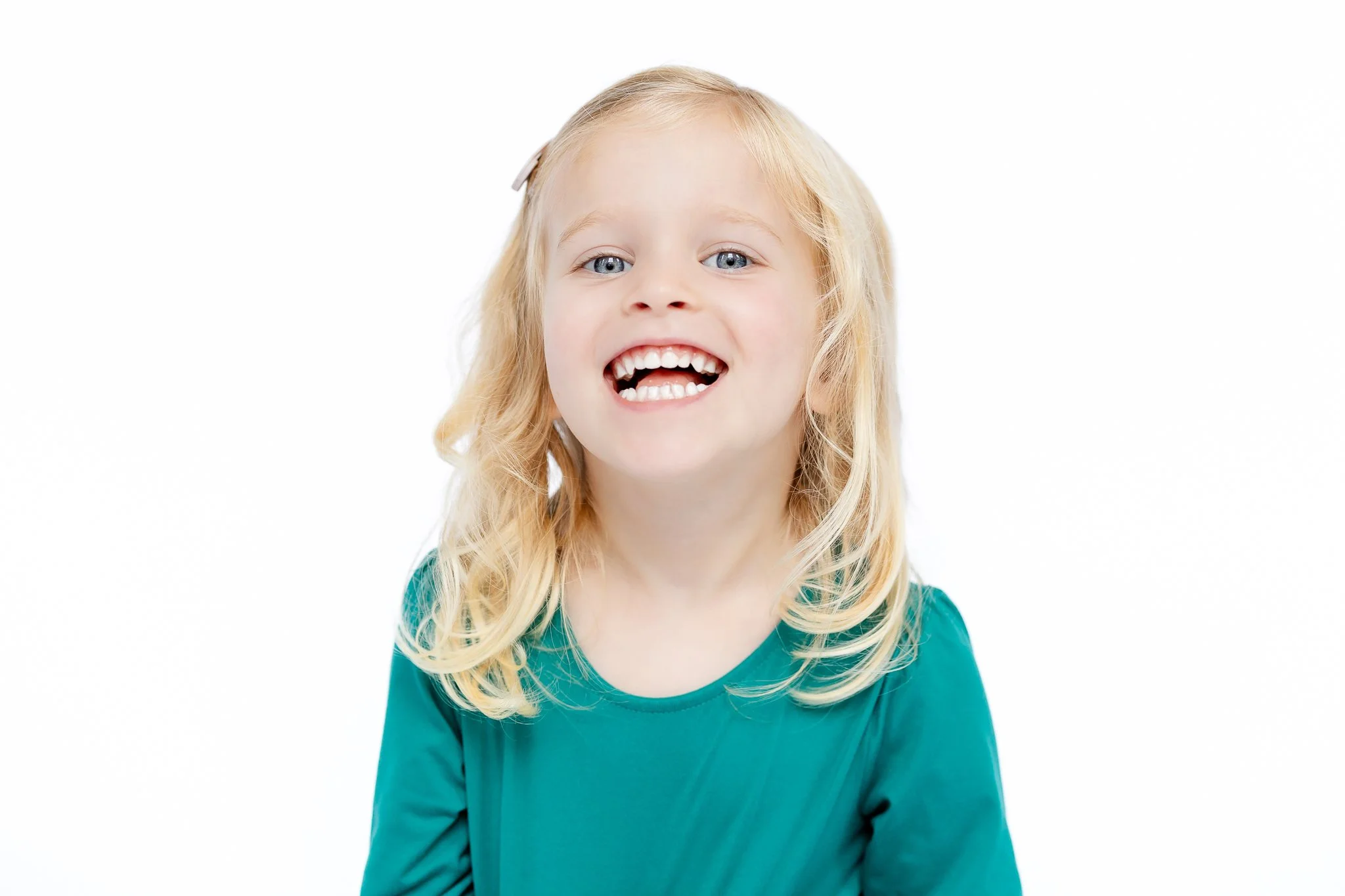 Smiling young girl with blonde hair and green shirt on white background.