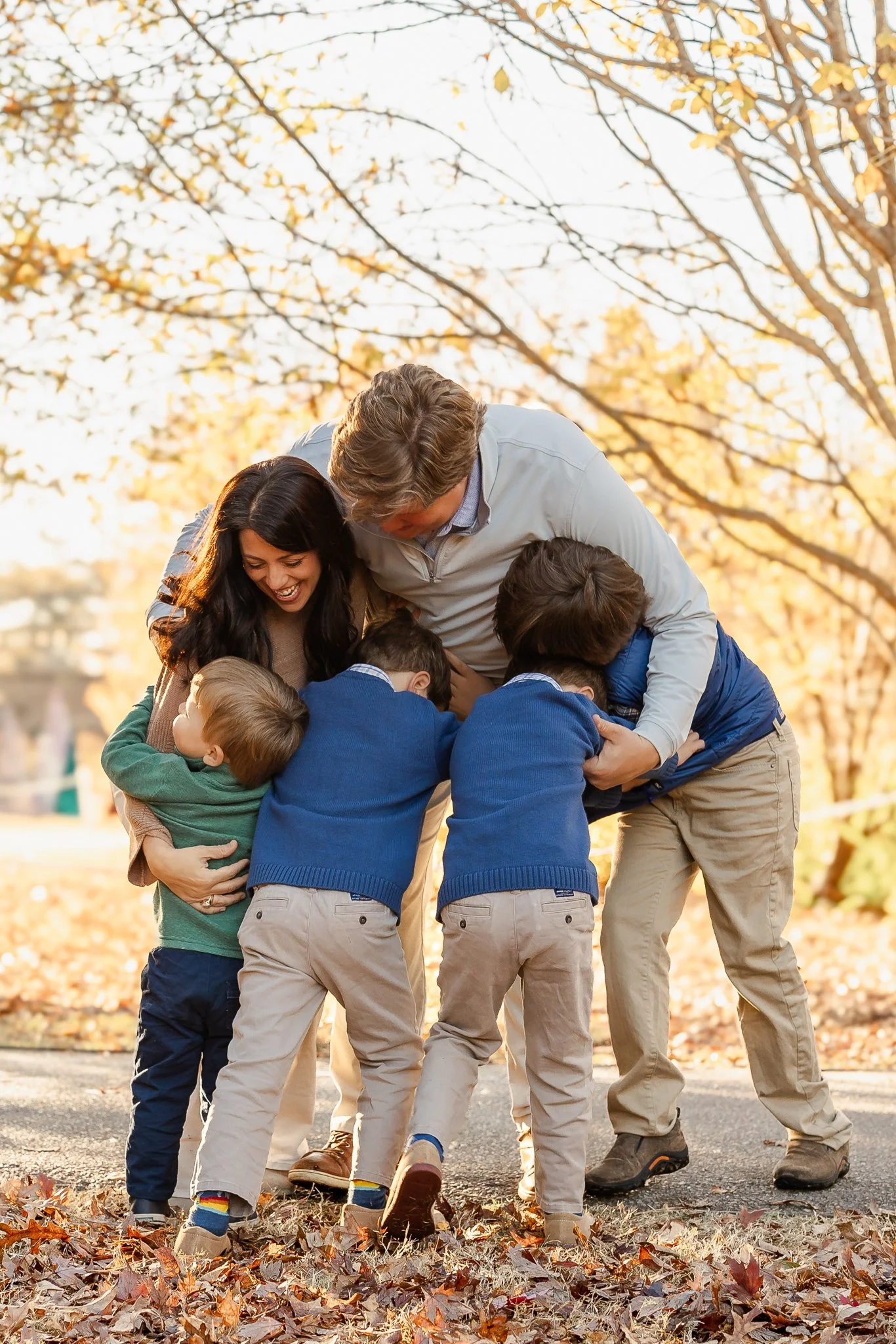 Family hugging outdoors during fall, surrounded by leaves.