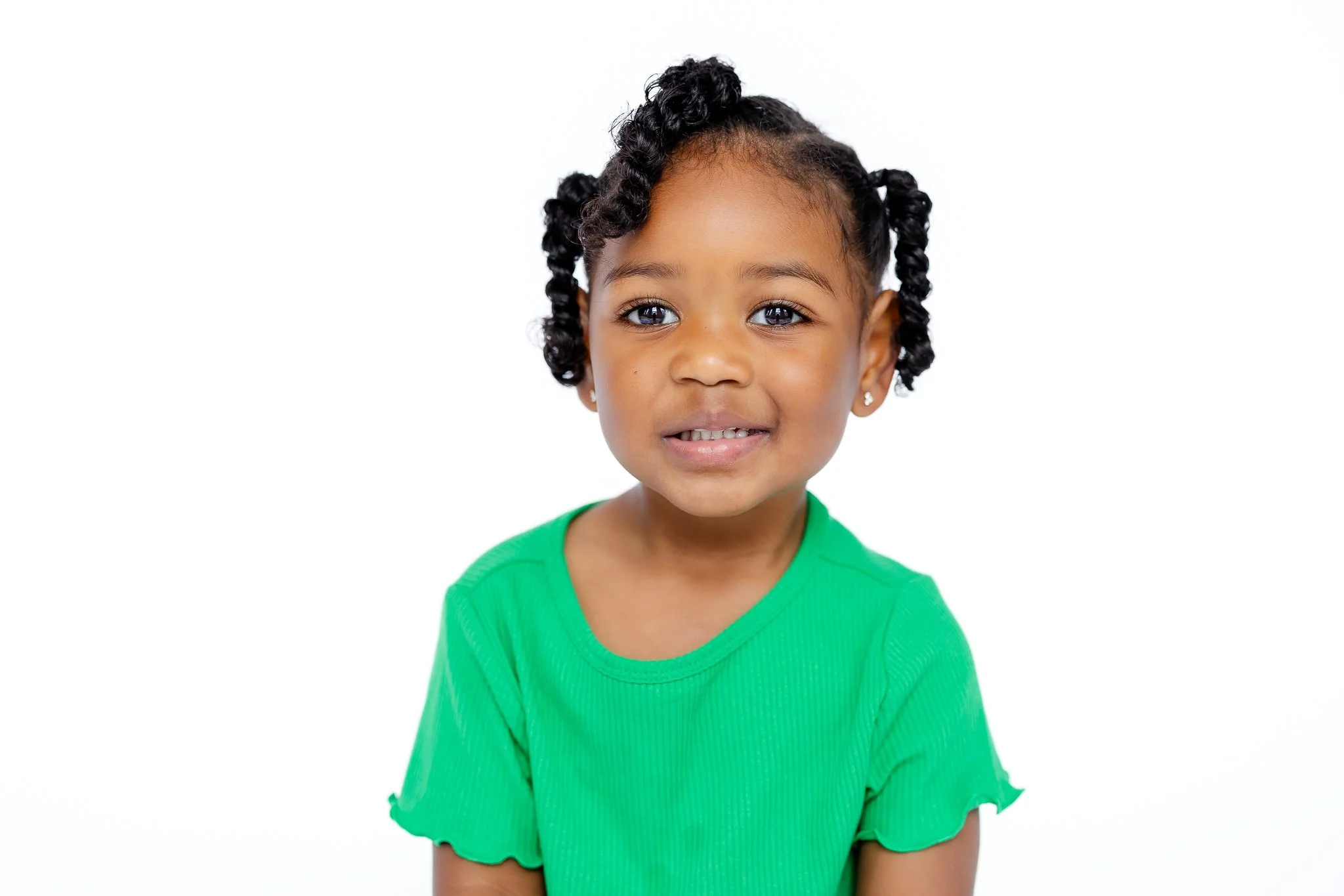 Young child in a green shirt smiling against a white background.