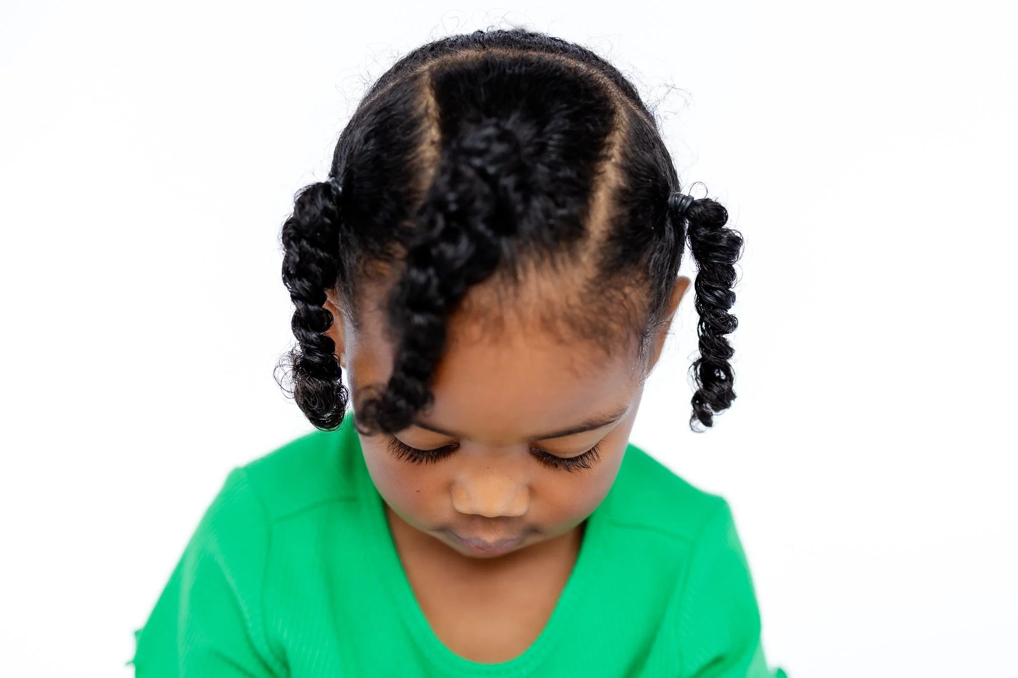 Young child with curly hair in a green shirt looking down.