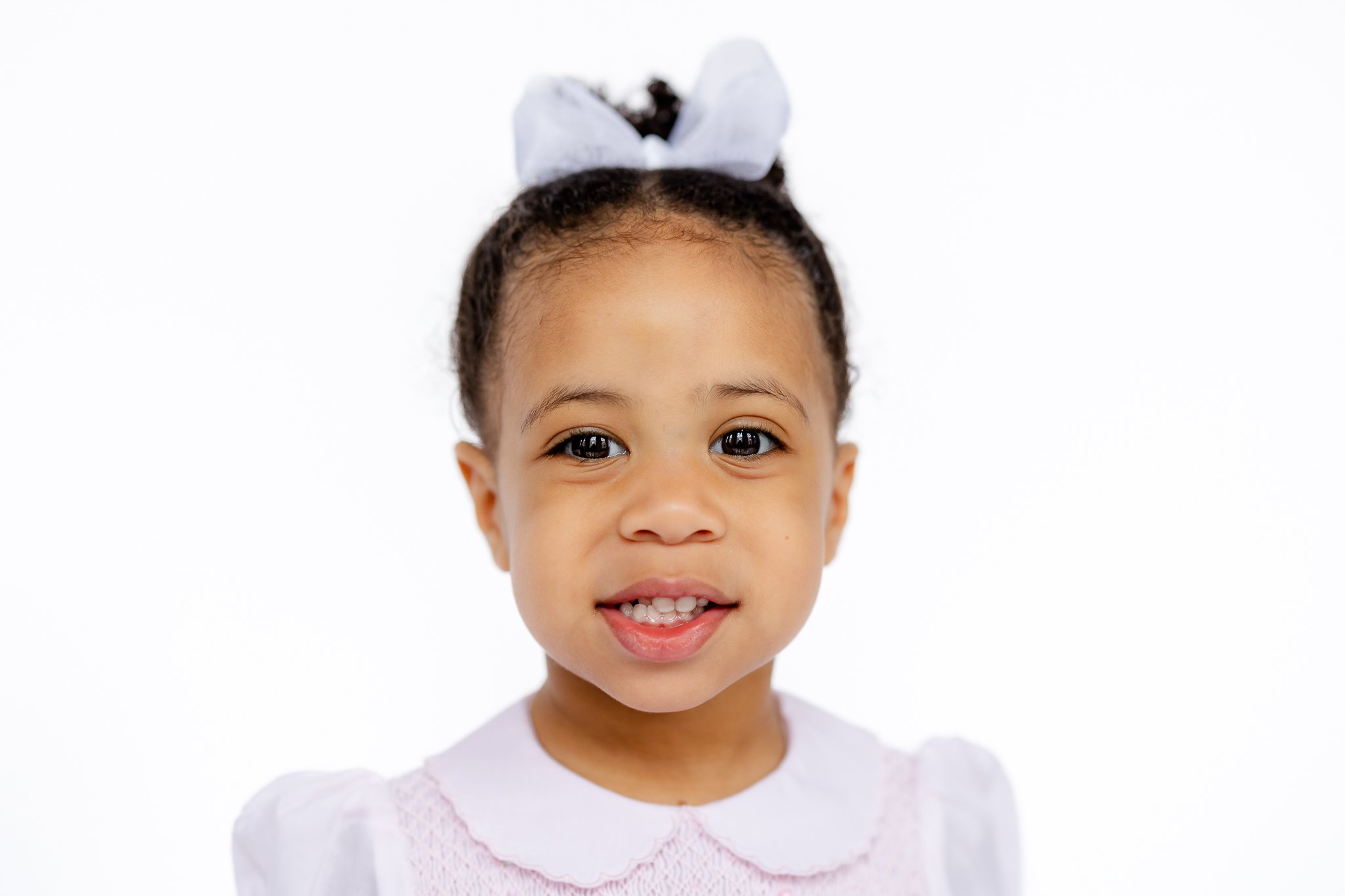 Portrait of a young girl with a white bow and white dress, smiling.