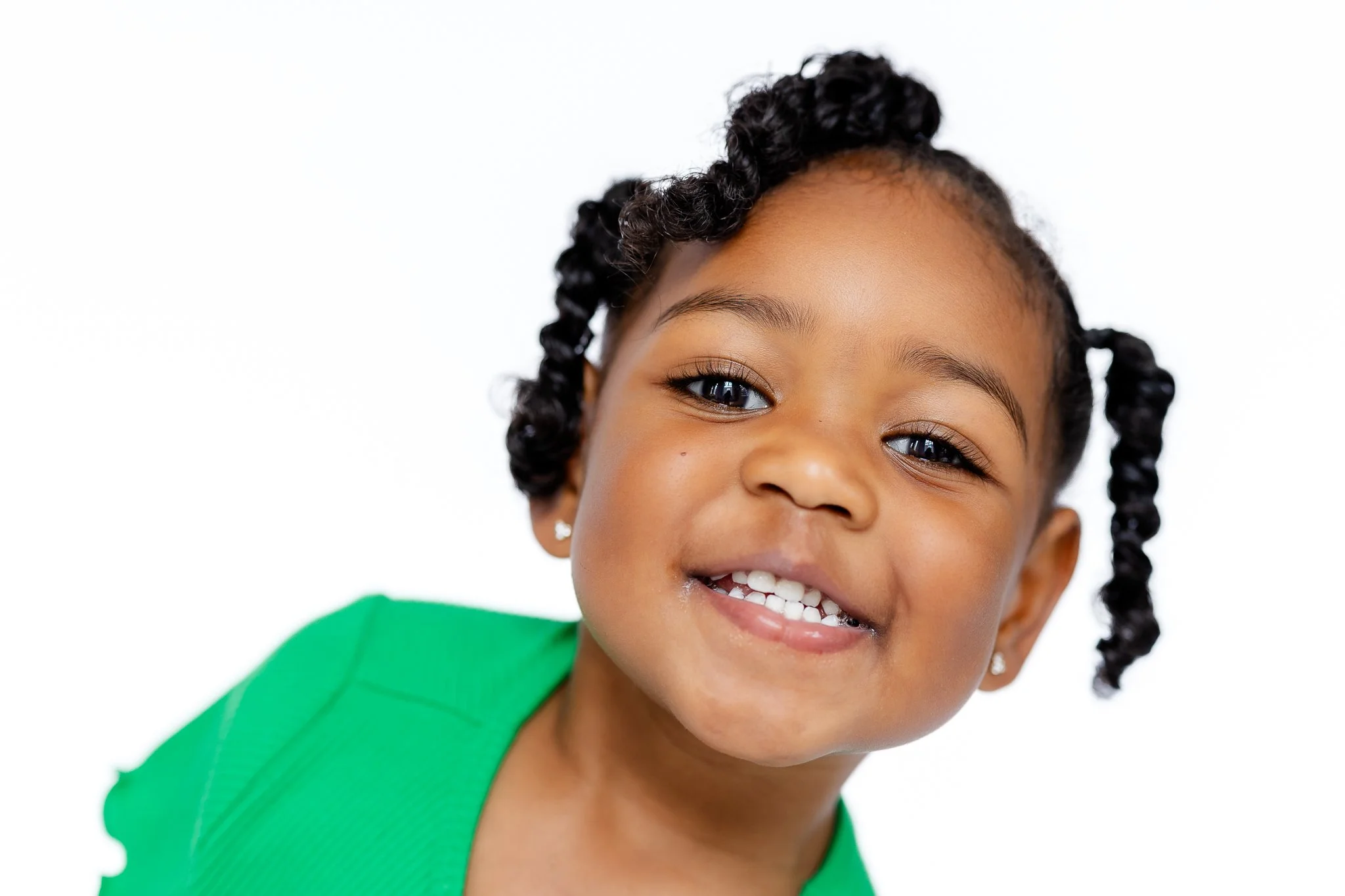 Close-up of a smiling child with curly hair wearing a green outfit.