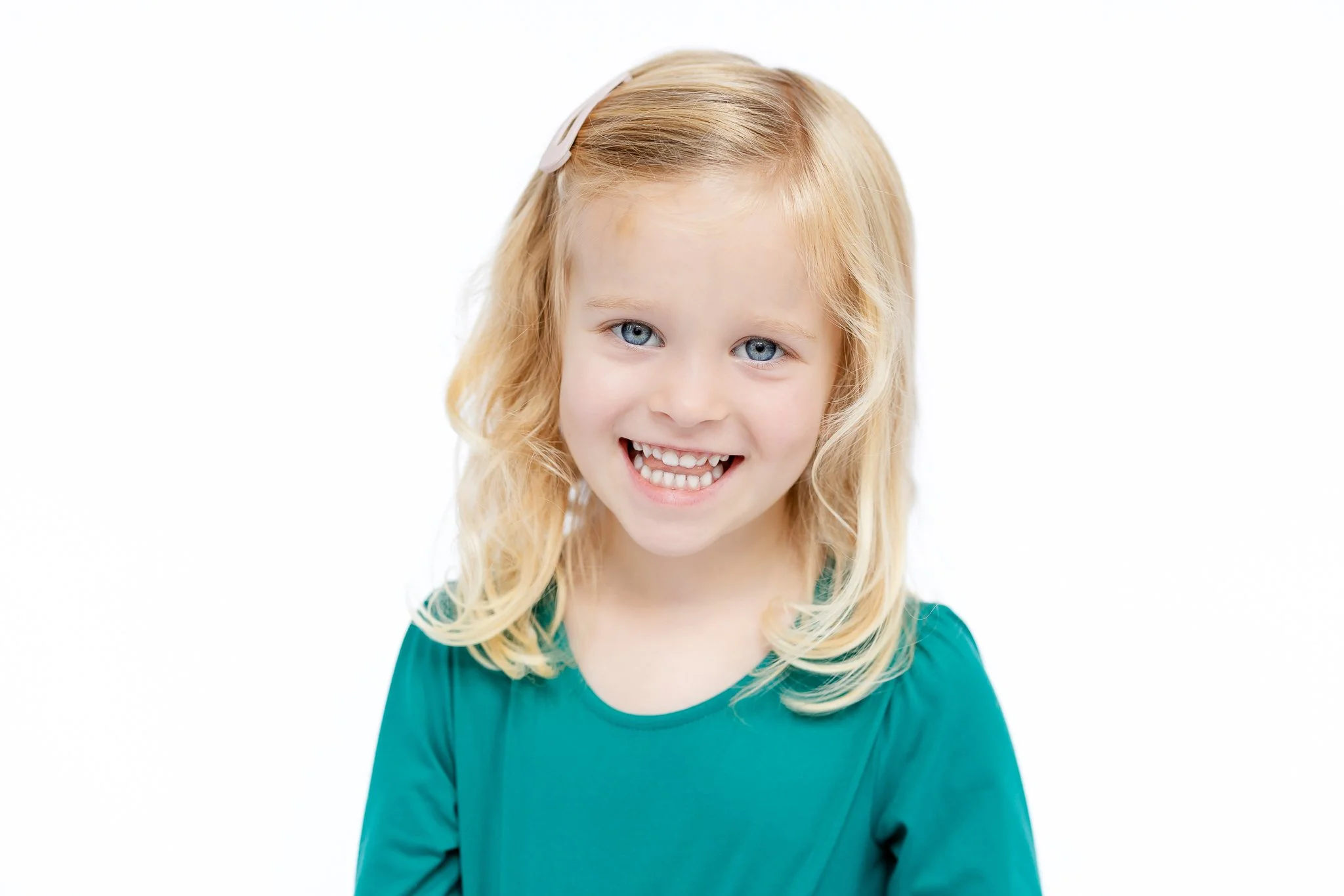 Smiling young girl with blonde hair and teal shirt on white background.
