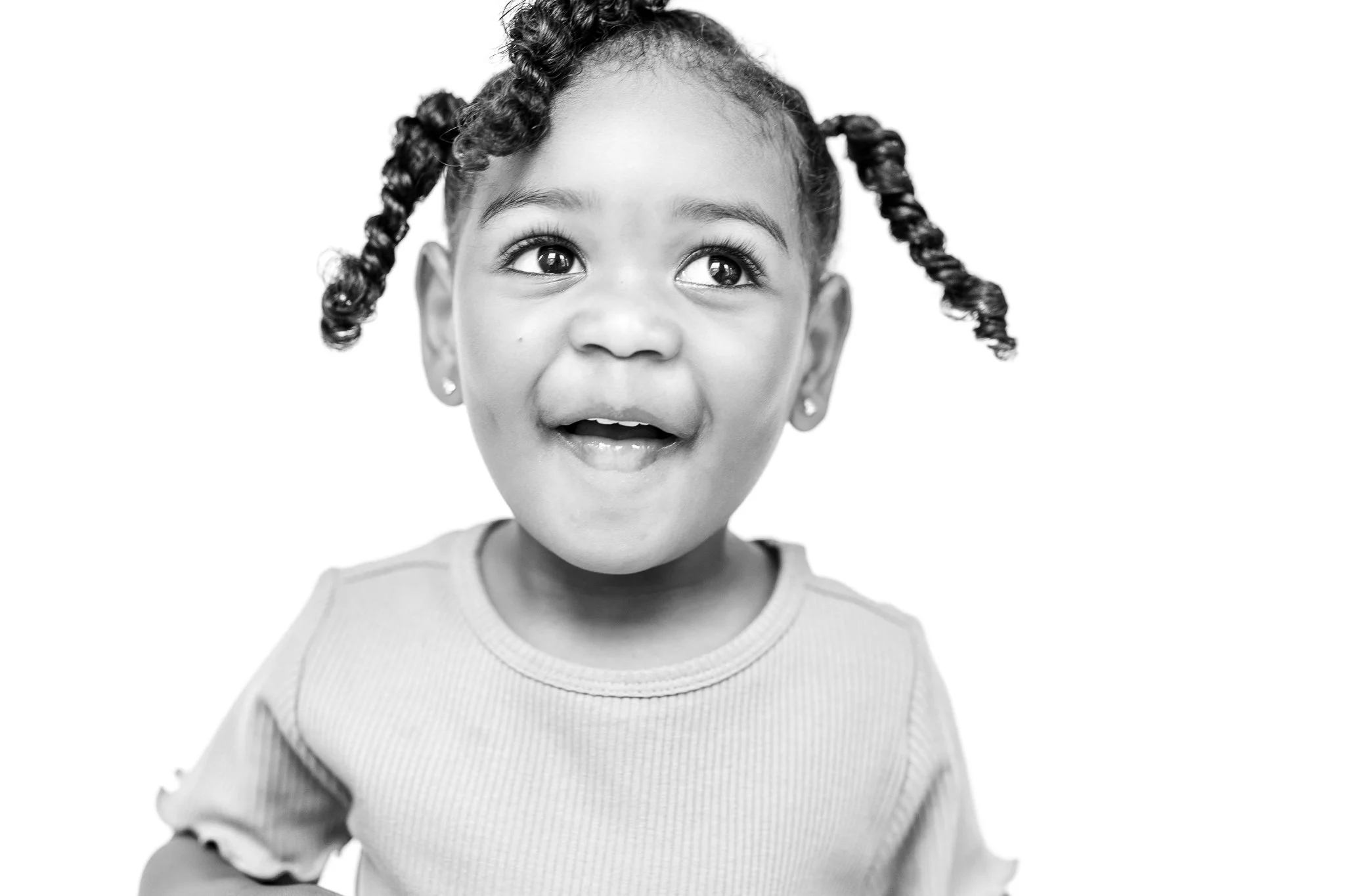Black and white photo of a smiling child with curly hair in pigtails.