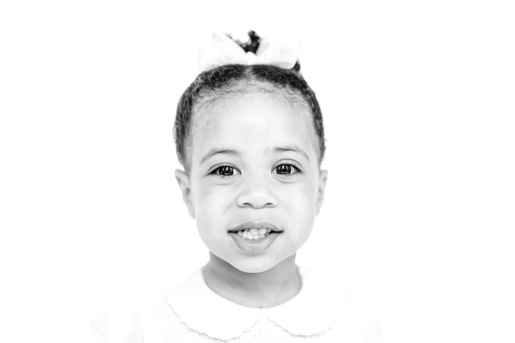 Black and white portrait of a smiling child with a bow in their hair.