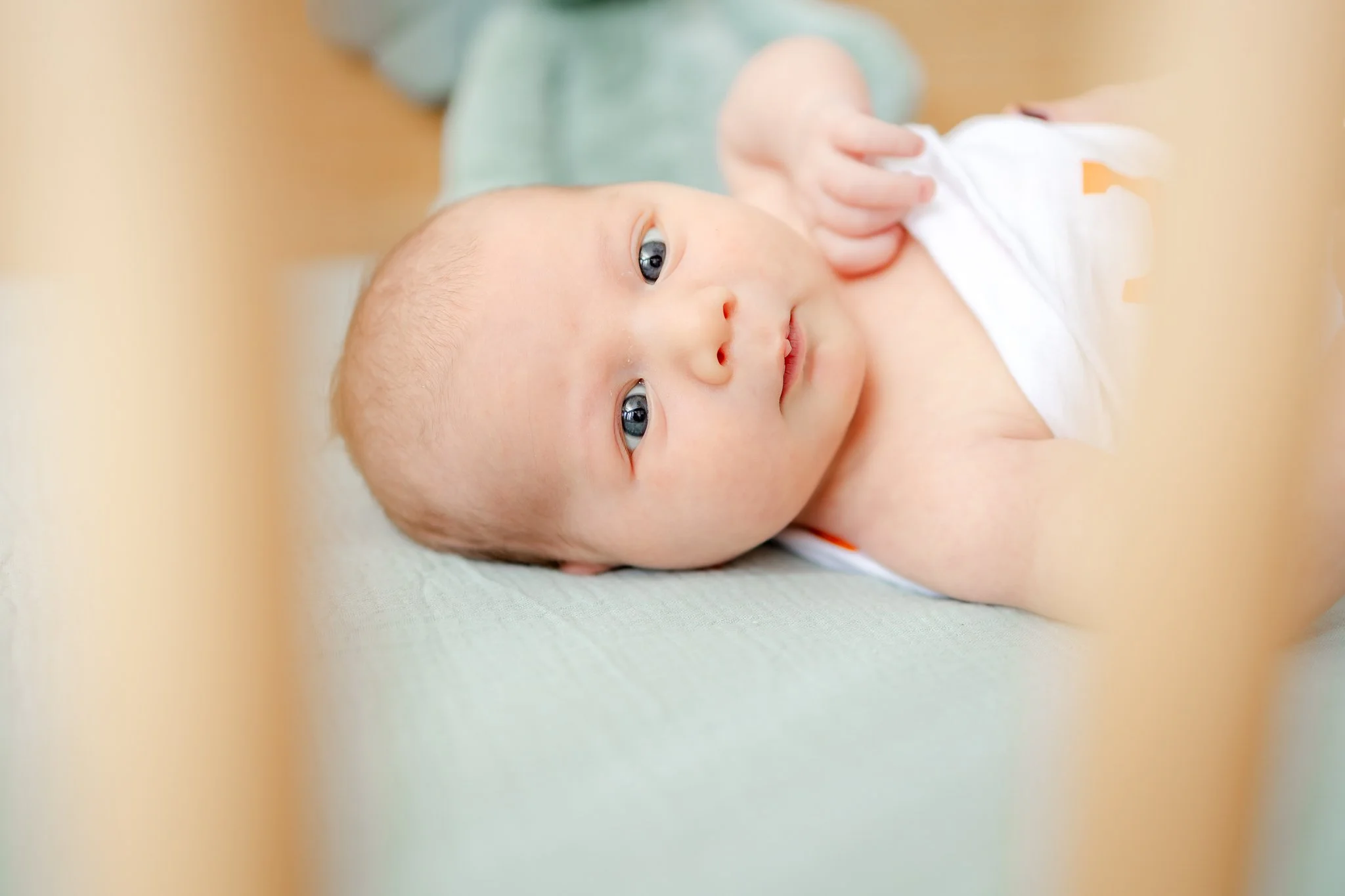Close-up of a baby lying on a light blue blanket, looking upwards with a curious expression.
