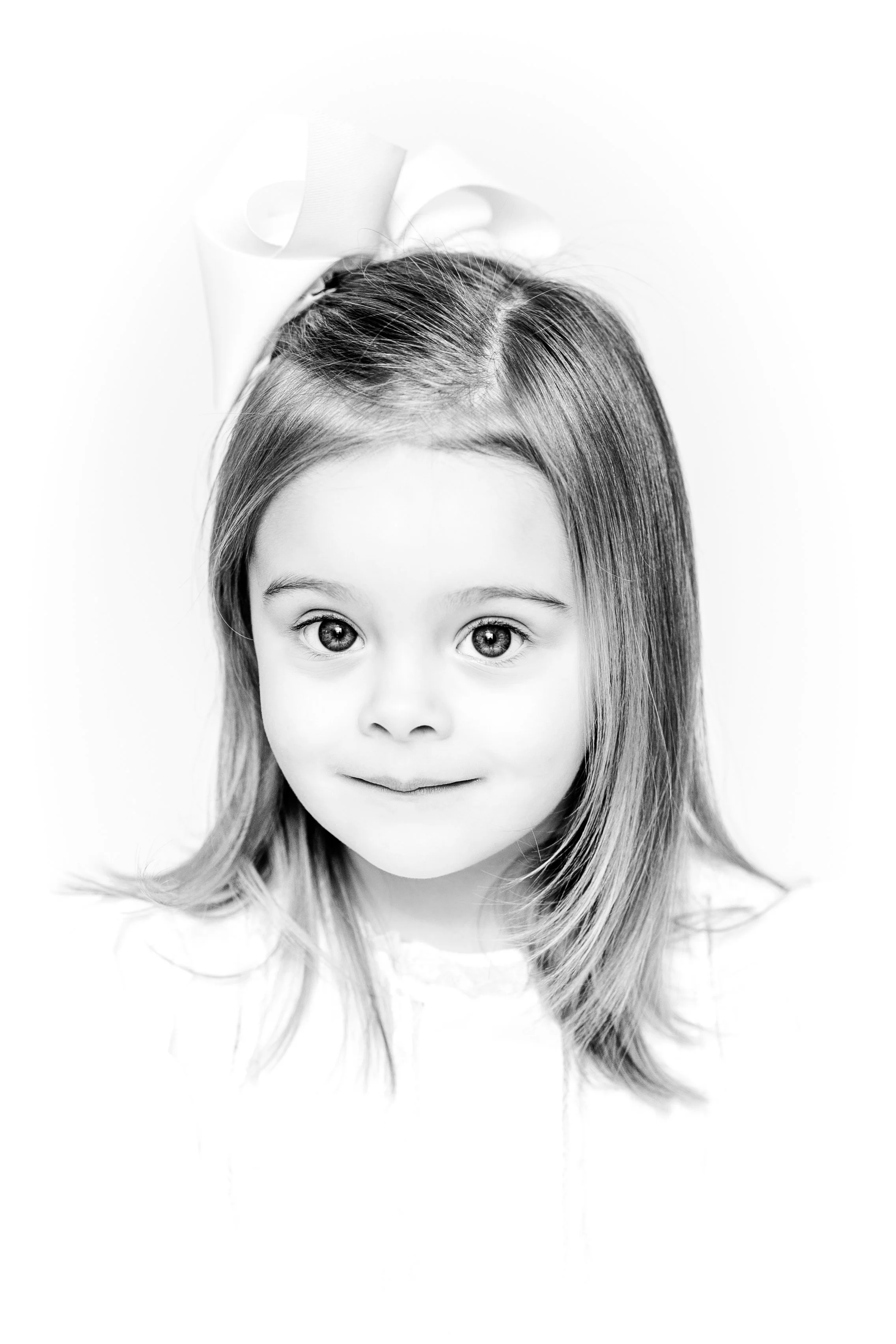 Black and white portrait of a young girl with a bow in her hair, smiling softly.