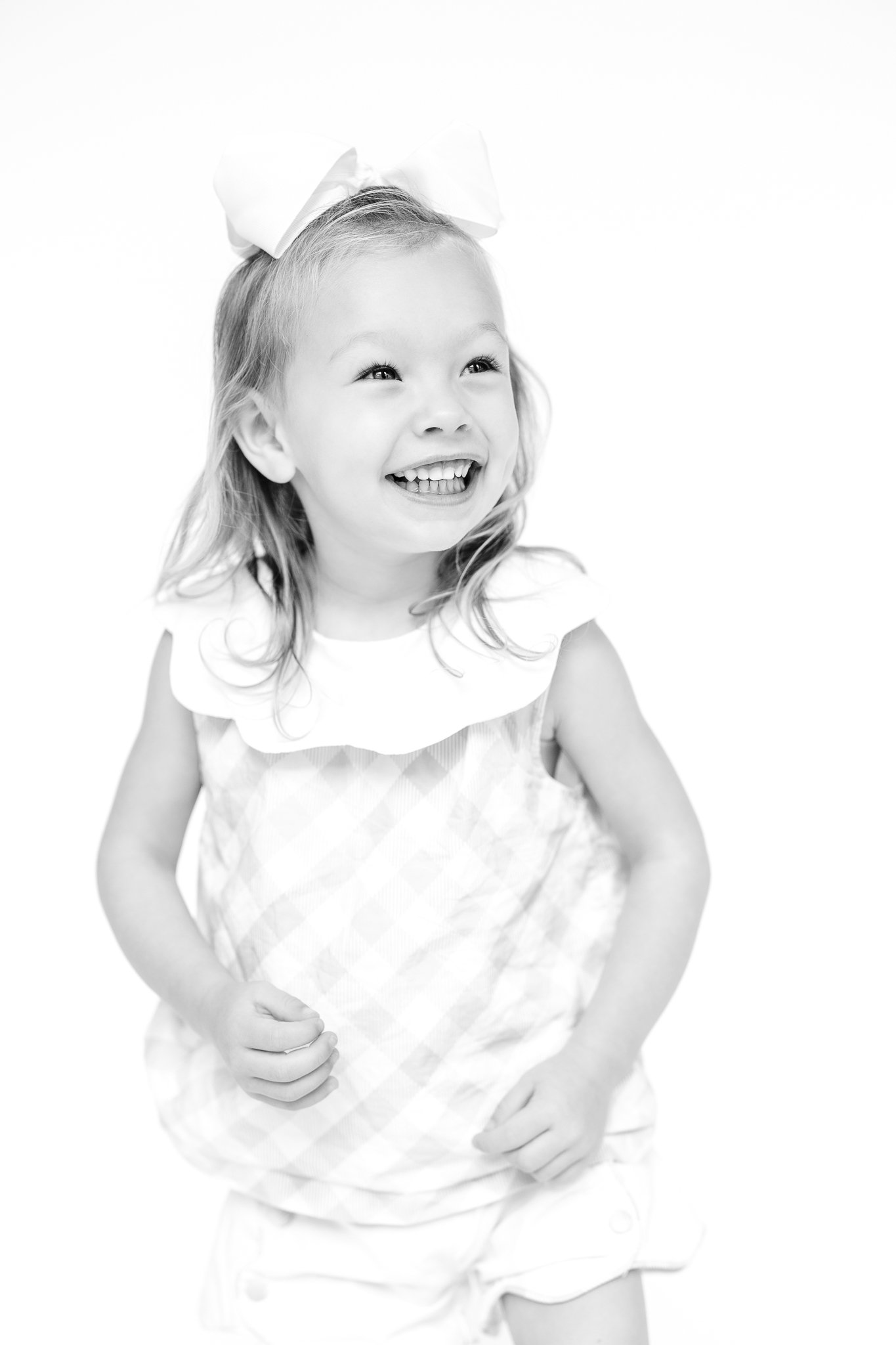 Smiling young girl with a bow in her hair, wearing a checkered dress.