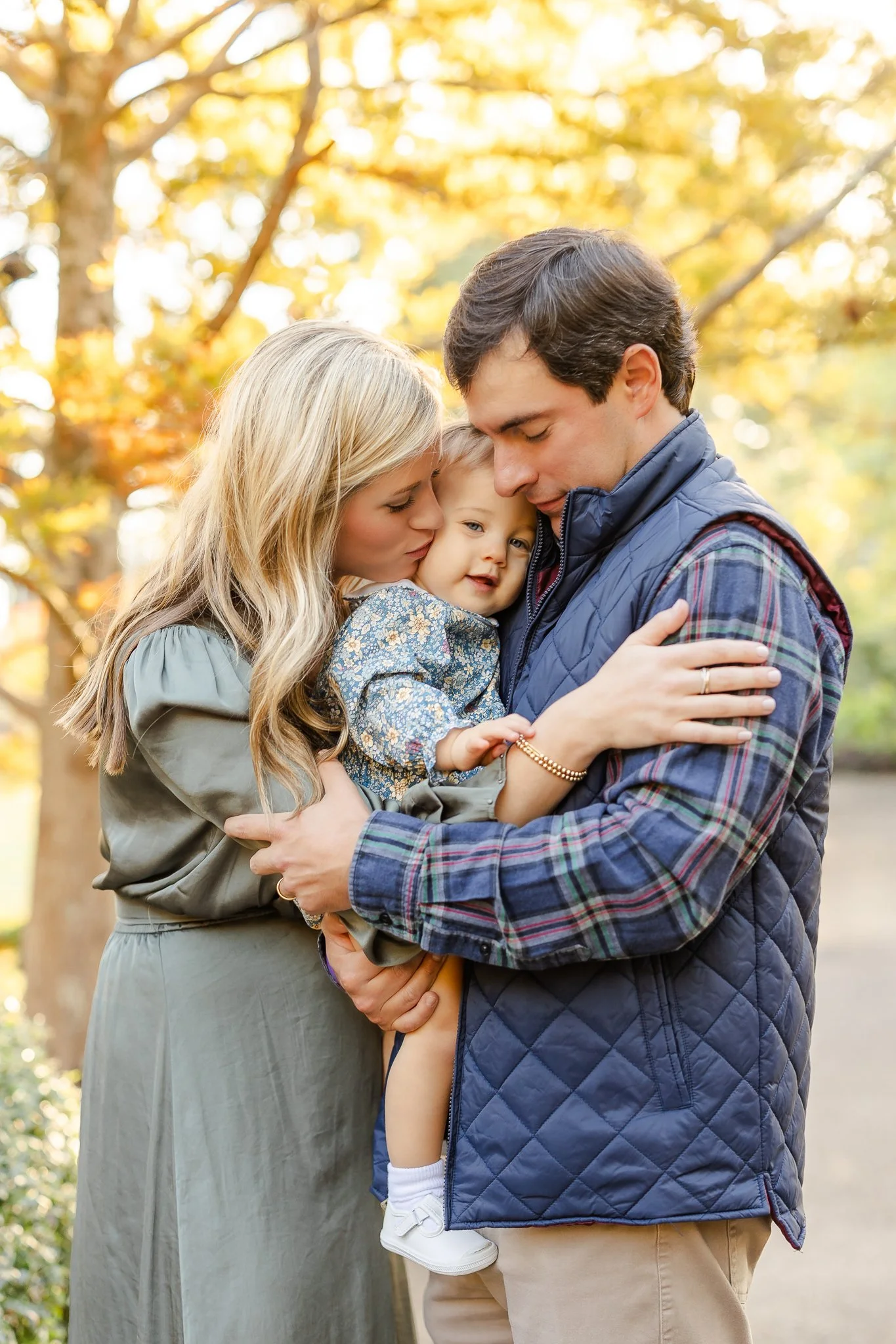 Couple embracing child during Family Photography session using Natural Light with fall foliage by Caitlin Ross in Memphis Tennessee