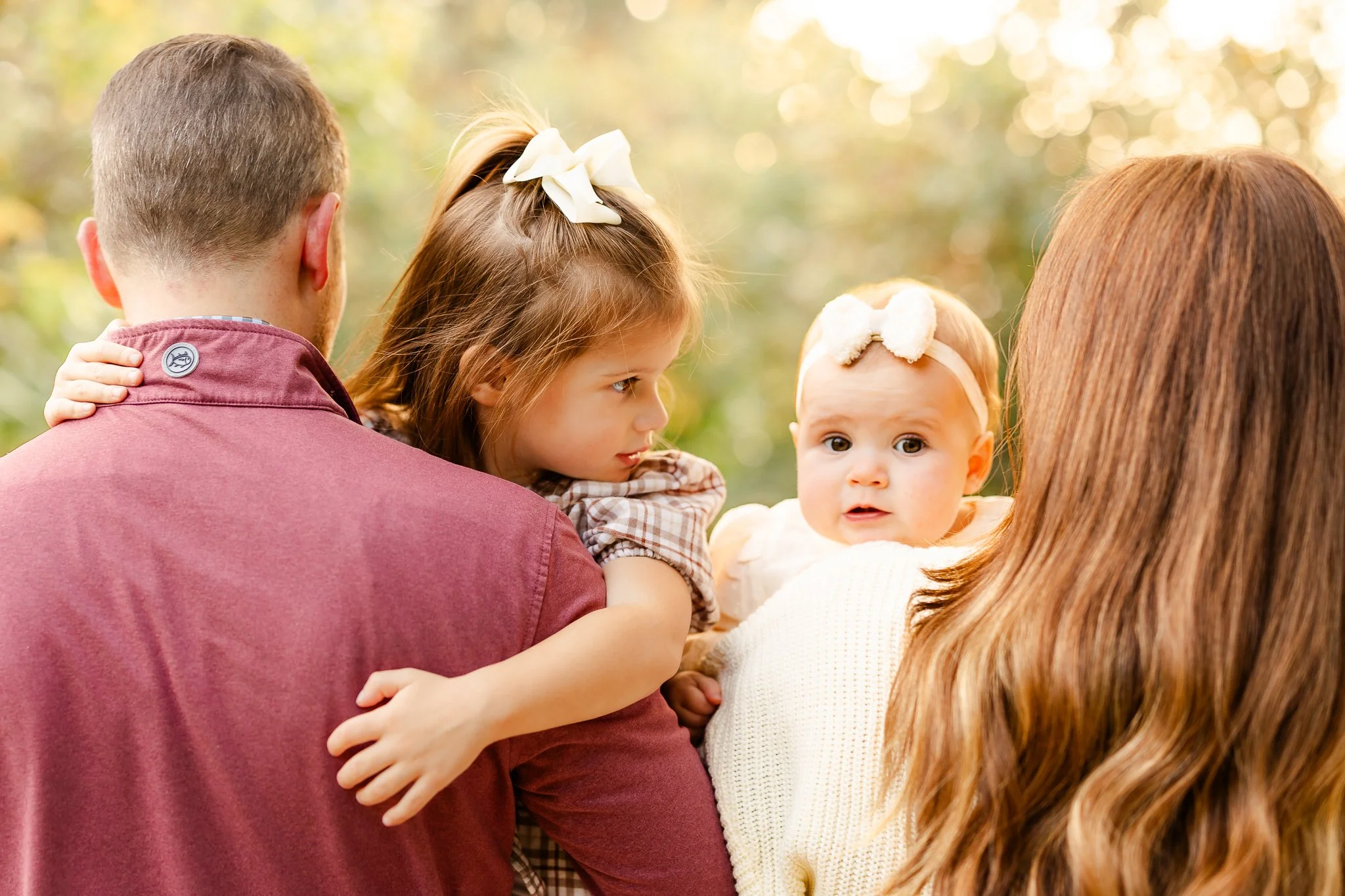 Family holding two children outdoors, autumn setting.